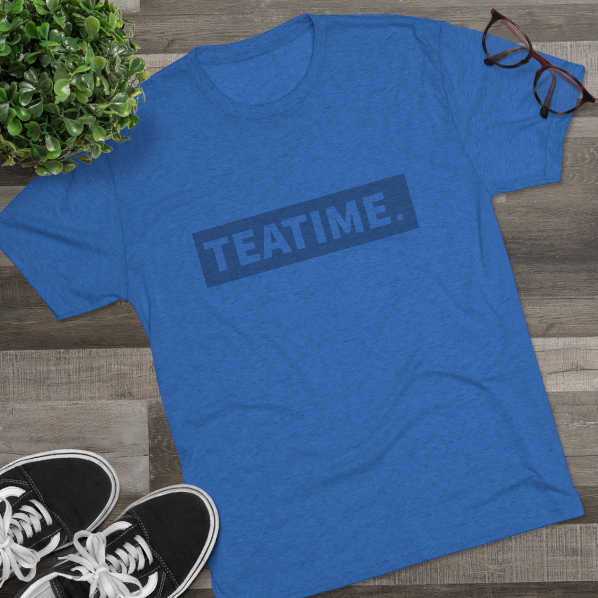 Blue graphic tee featuring the word "TEATIME." in bold text, styled with casual sneakers and glasses.