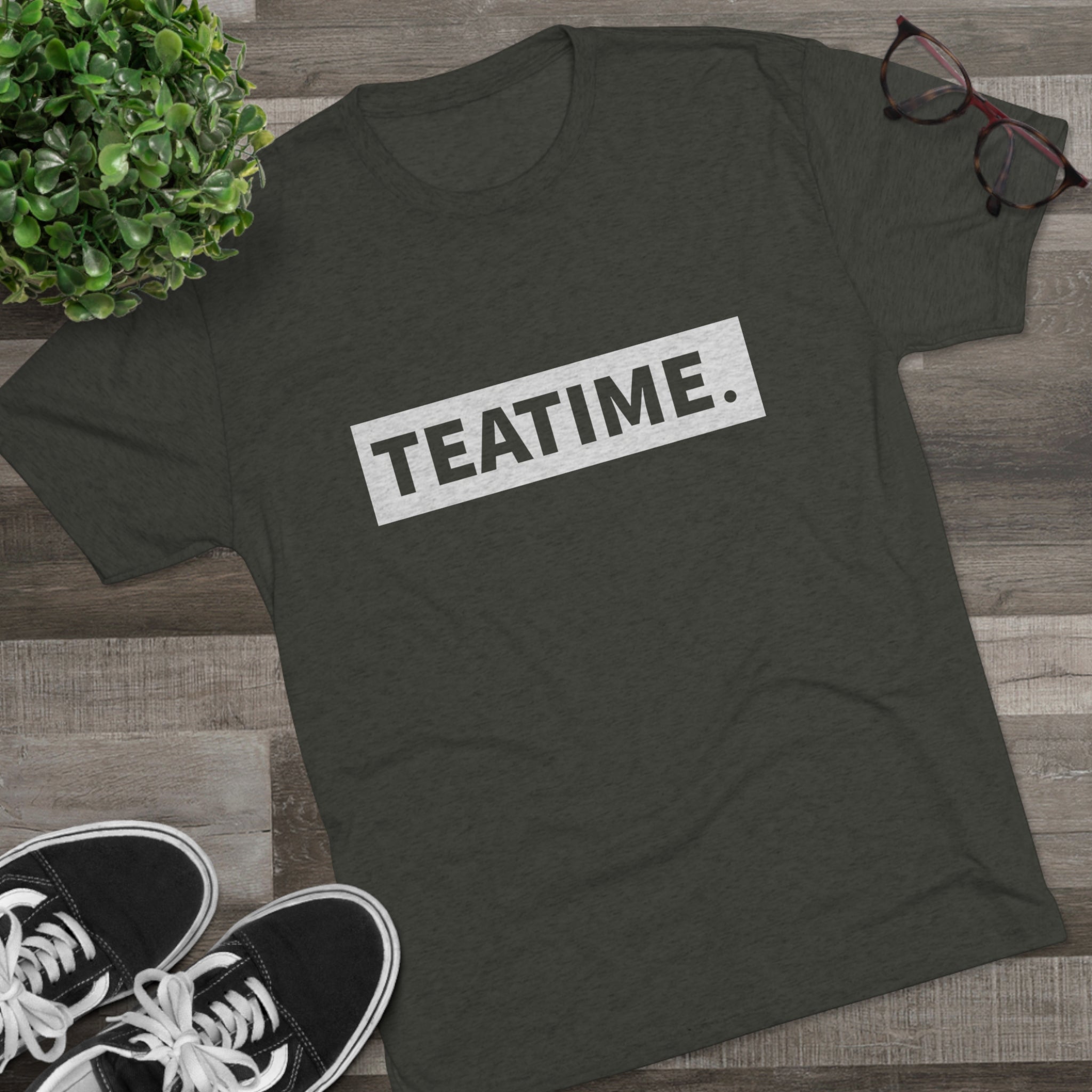 Olive green graphic tee featuring the word "TEATIME." in bold white letters, styled with casual sneakers and glasses.