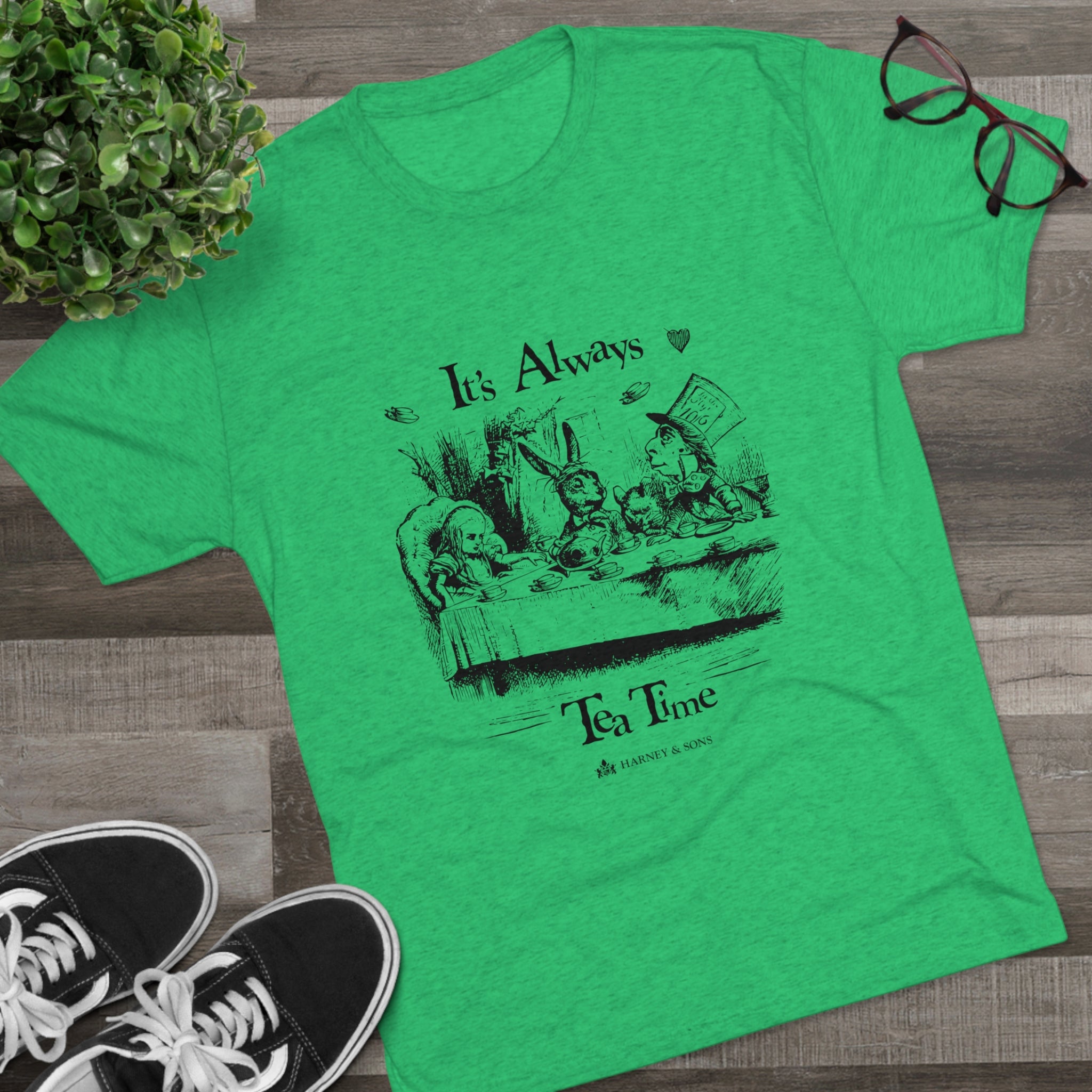 Green graphic tee featuring "It's Always Tea Time" design with whimsical characters at a tea party.