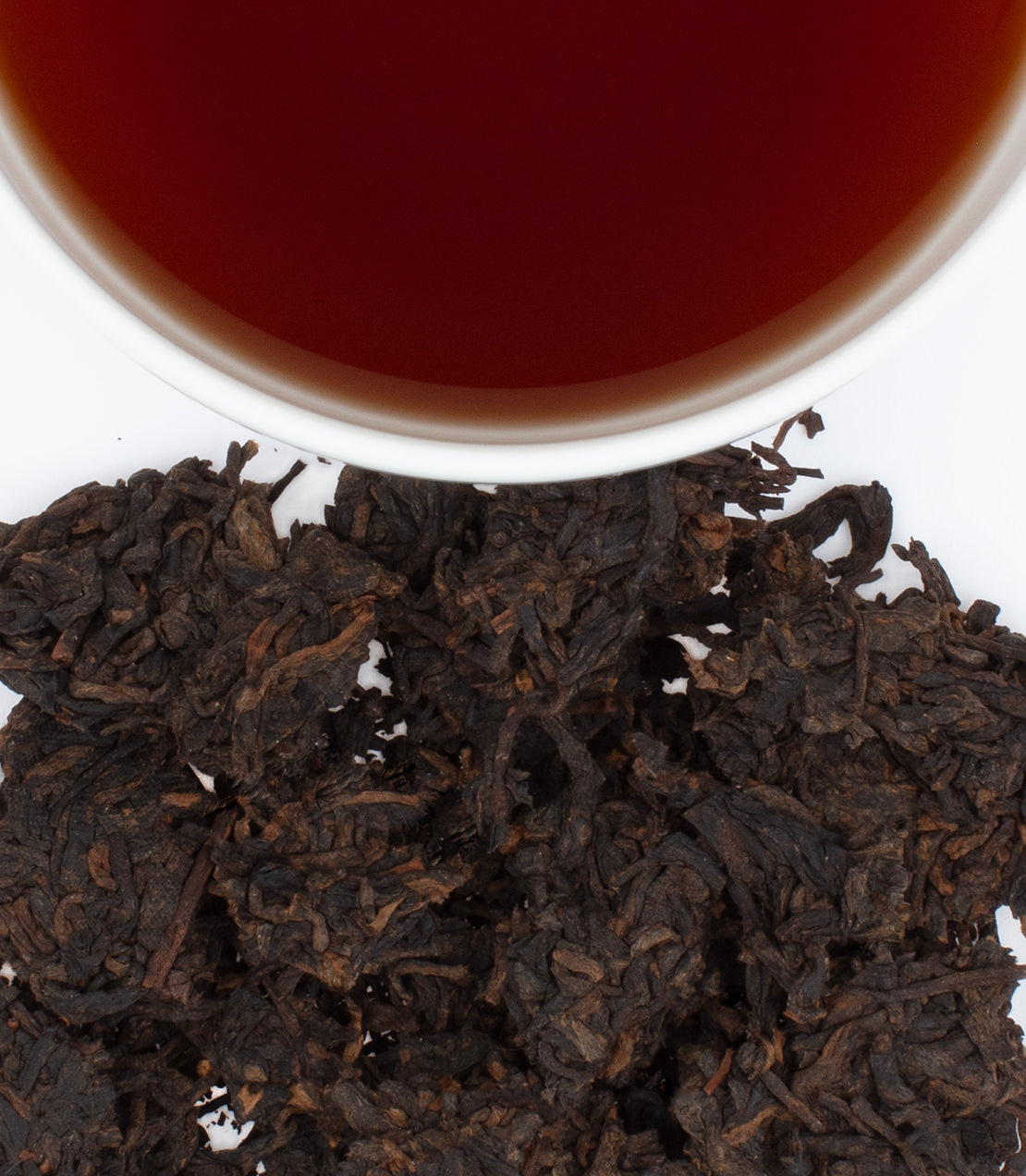 2018 Ripe Pu-Erh tea leaves beside a cup of deep reddish-brown brewed tea, showcasing rich color and texture.