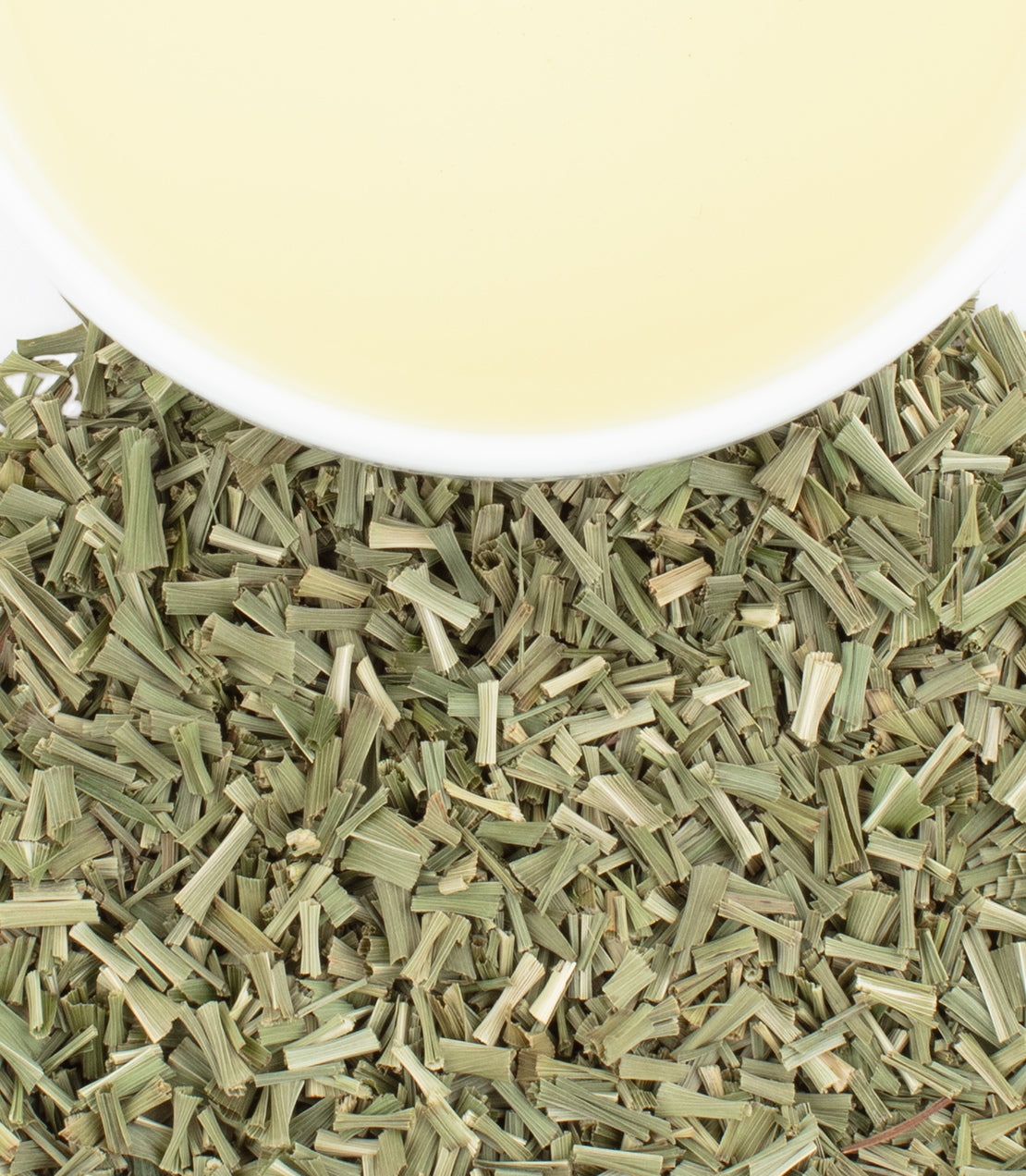 Dried Amba lemongrass leaves with a bowl of light yellow lemongrass tea on a white background.