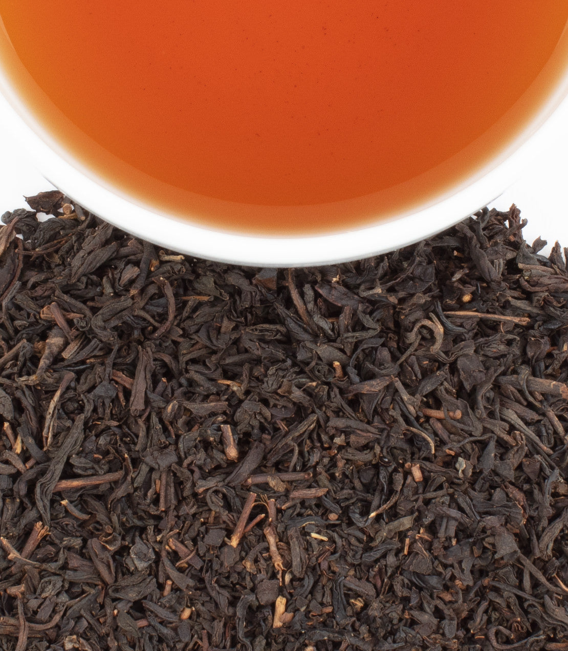 A cup of brewed chocolate tea above loose black tea leaves, showcasing a rich amber color.