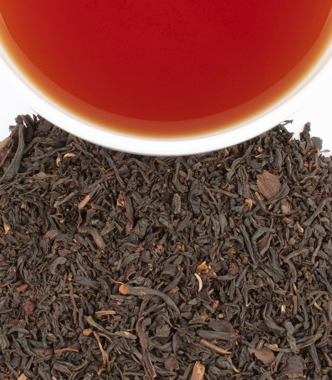 A cup of citrus blend tea above a pile of loose black tea leaves, showcasing rich colors and textures.