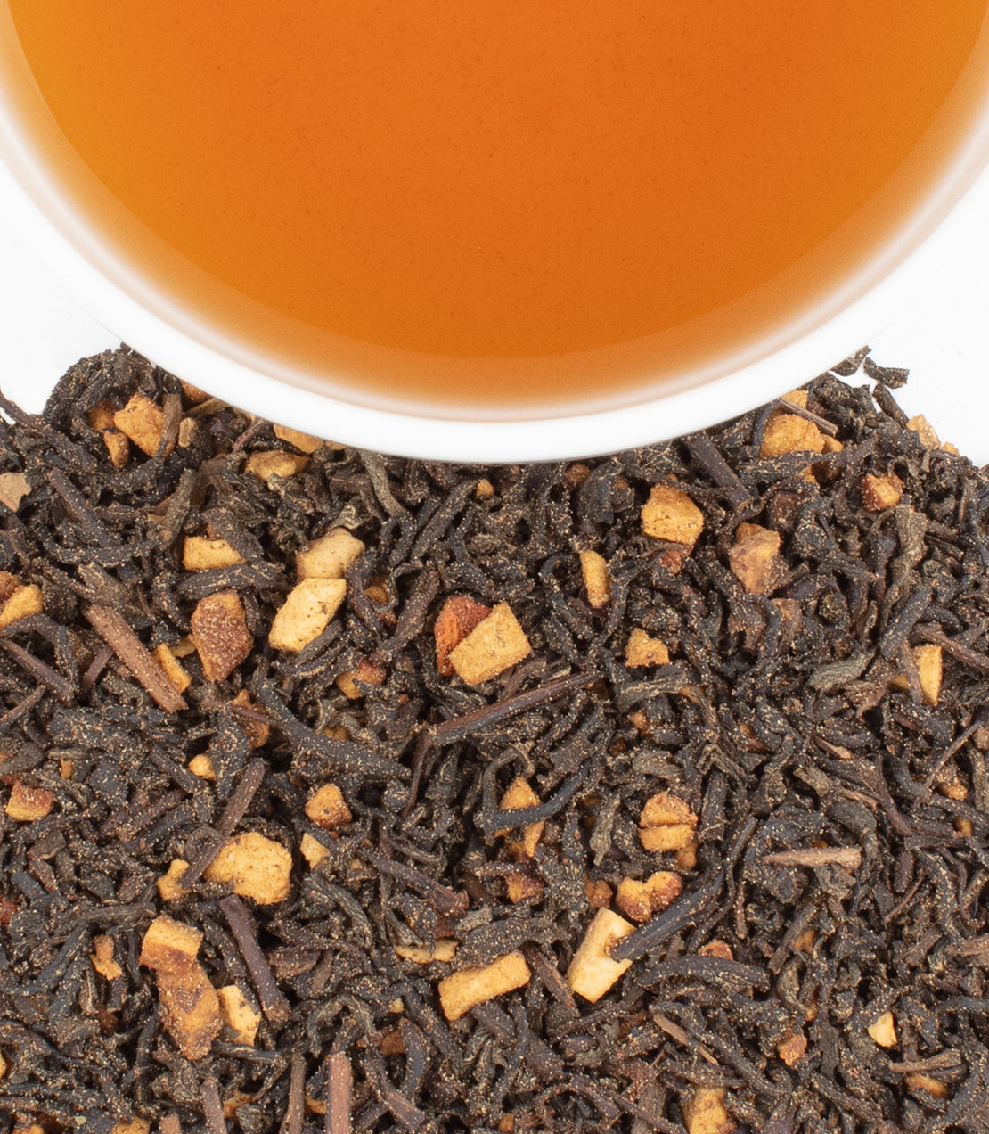 A close-up of decaf hot cinnamon tea leaves with a cup of brewed tea above, showcasing rich colors and textures.
