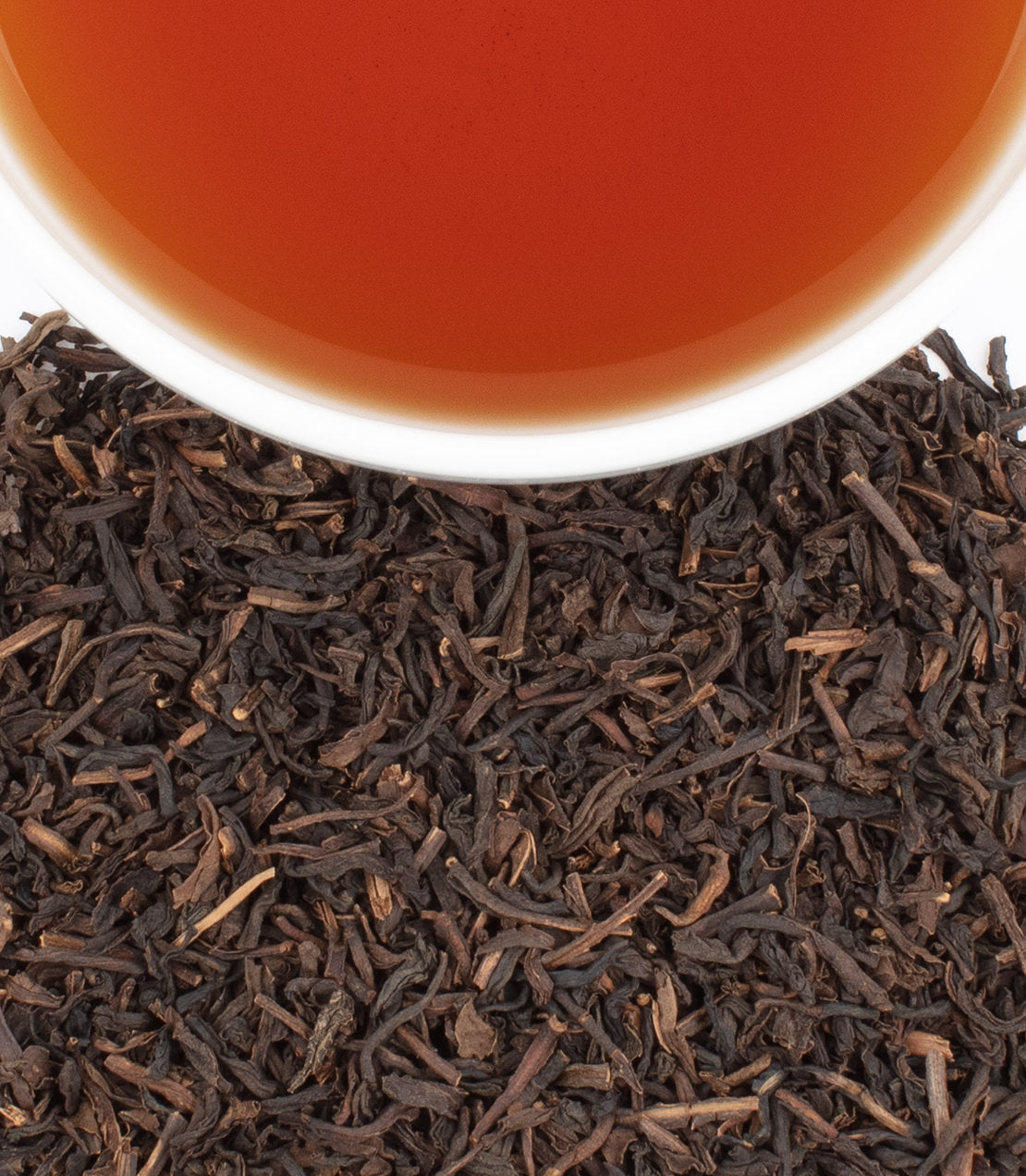 A cup of brewed Decaf Peaches & Ginger tea above loose black tea leaves, showcasing its rich amber color.