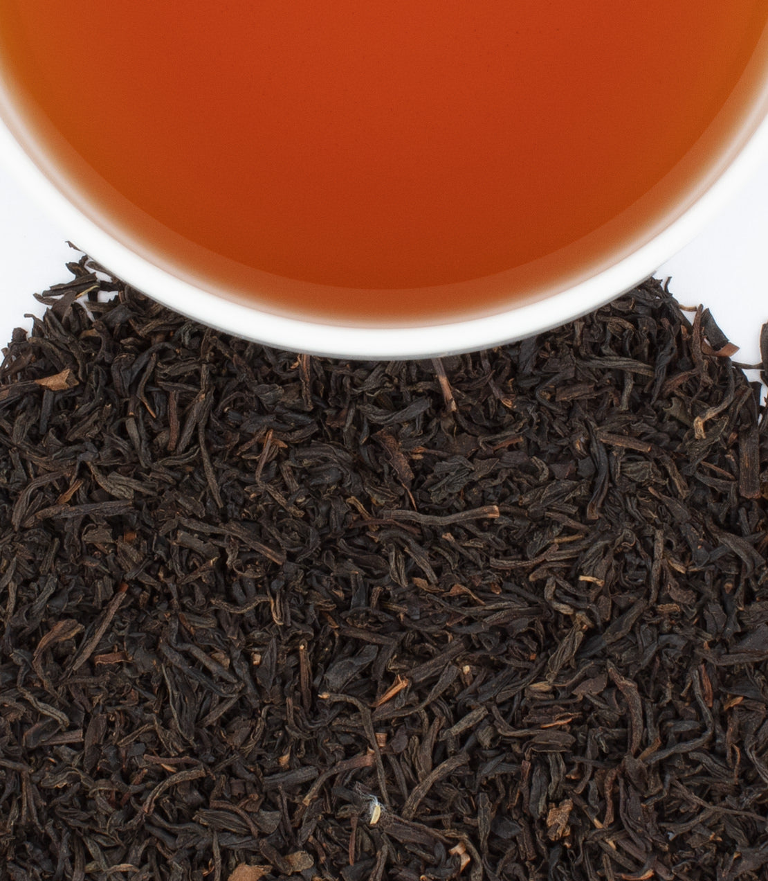 Classic English Breakfast tea in a white cup, surrounded by loose black tea leaves. Perfect for a morning boost.