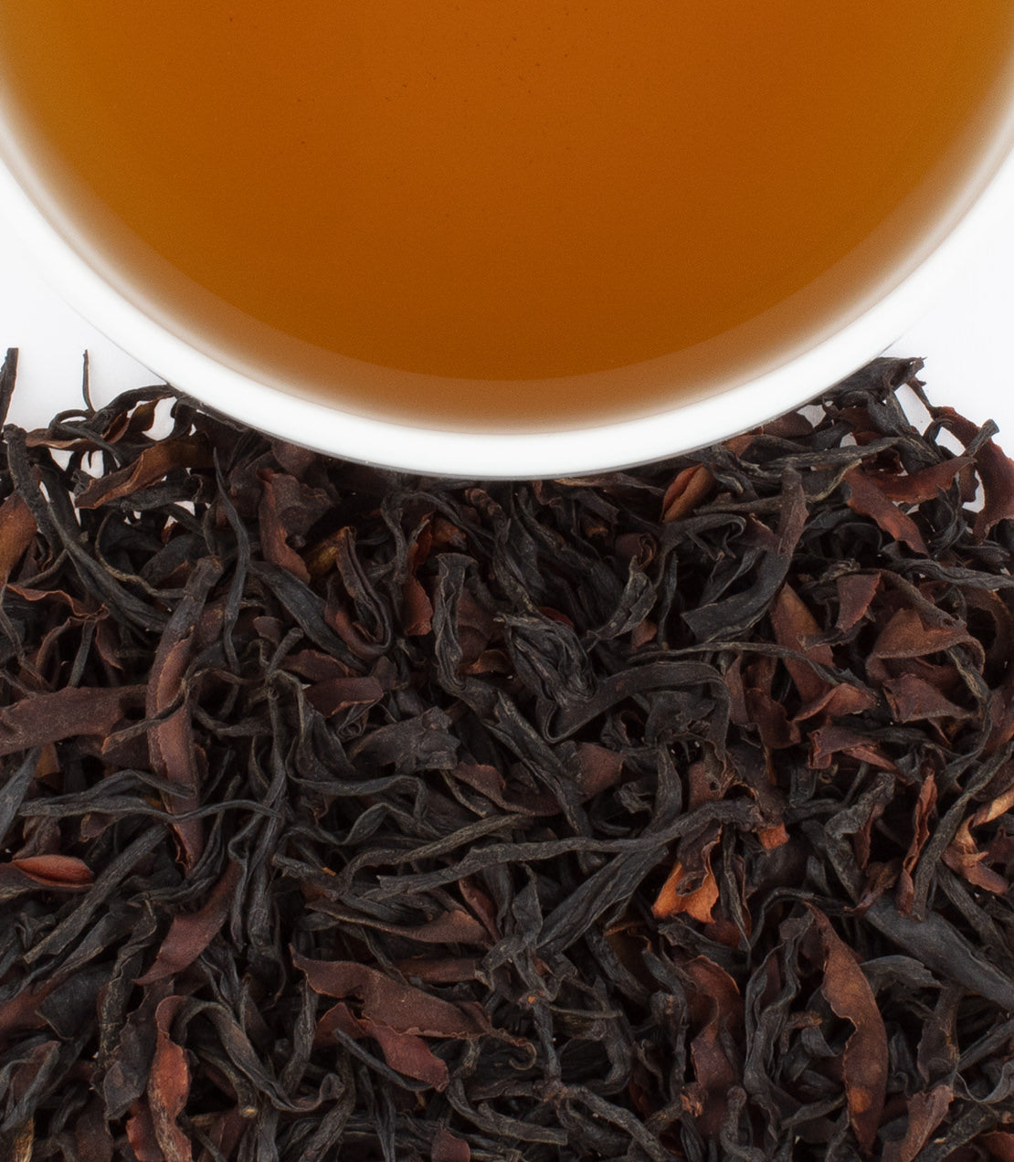 A close-up of Fujian Wild Black tea leaves beside a cup of brewed tea, showcasing rich colors and textures.