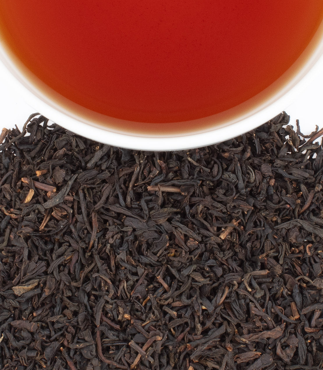 A close-up of loose black tea leaves with a cup of brewed salted caramel tea above, showcasing rich colors.