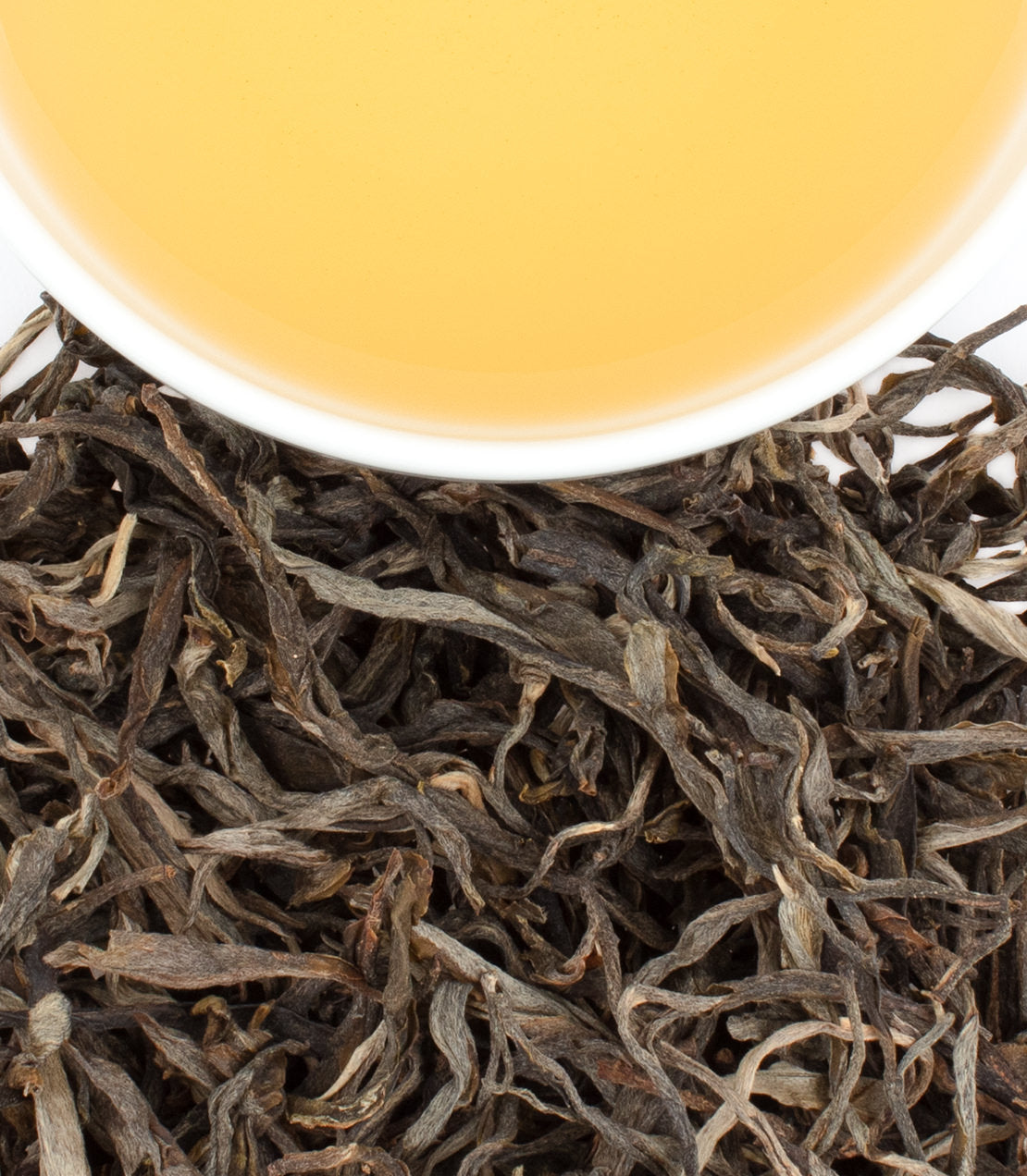 A cup of golden Pasha Raw Pu-Erh tea sits atop loose, dark tea leaves, showcasing its rich color and texture.