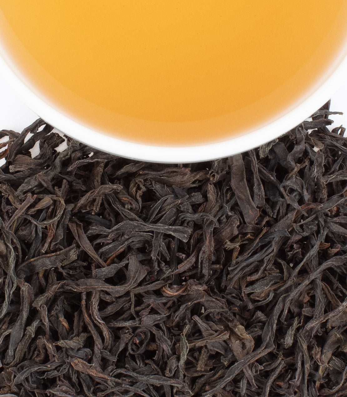 A cup of Phoenix Honey Orchid Oolong tea above loose dark tea leaves, showcasing its rich amber color.