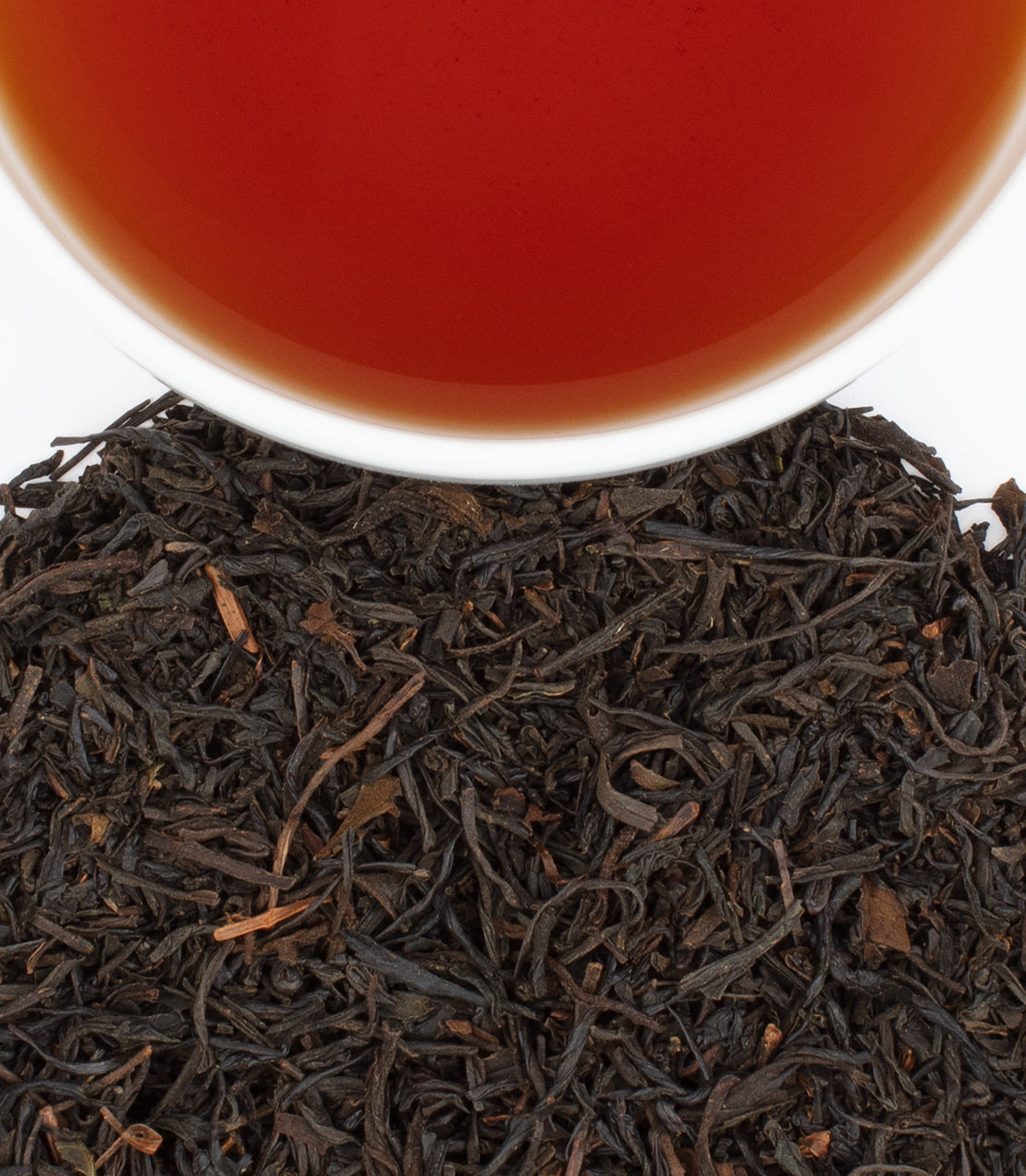A cup of Wazuka Black tea above a mound of loose black tea leaves, showcasing rich color and texture.