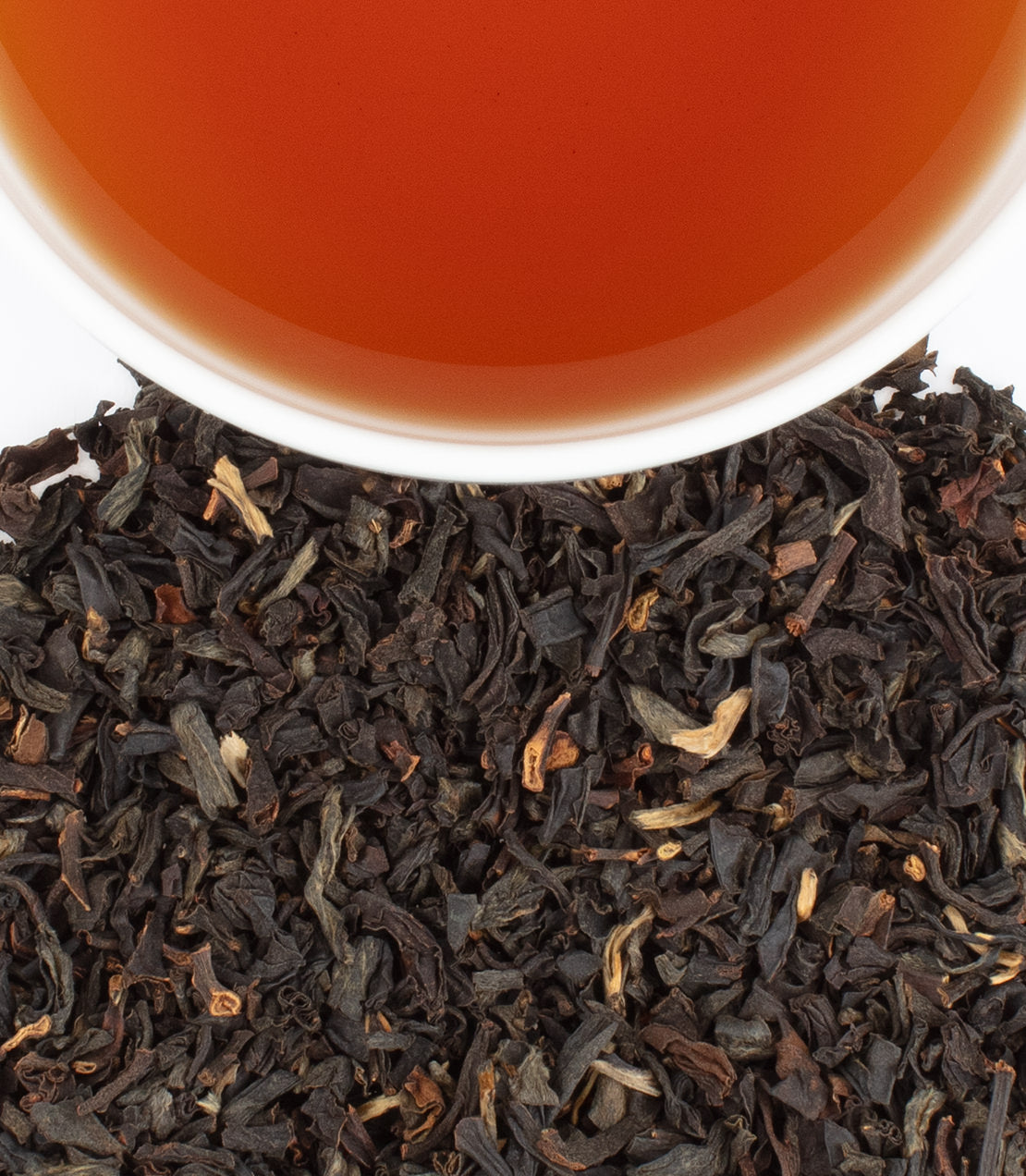 A cup of brewed Wild Ceylon Black tea above loose black tea leaves, showcasing rich color and texture.