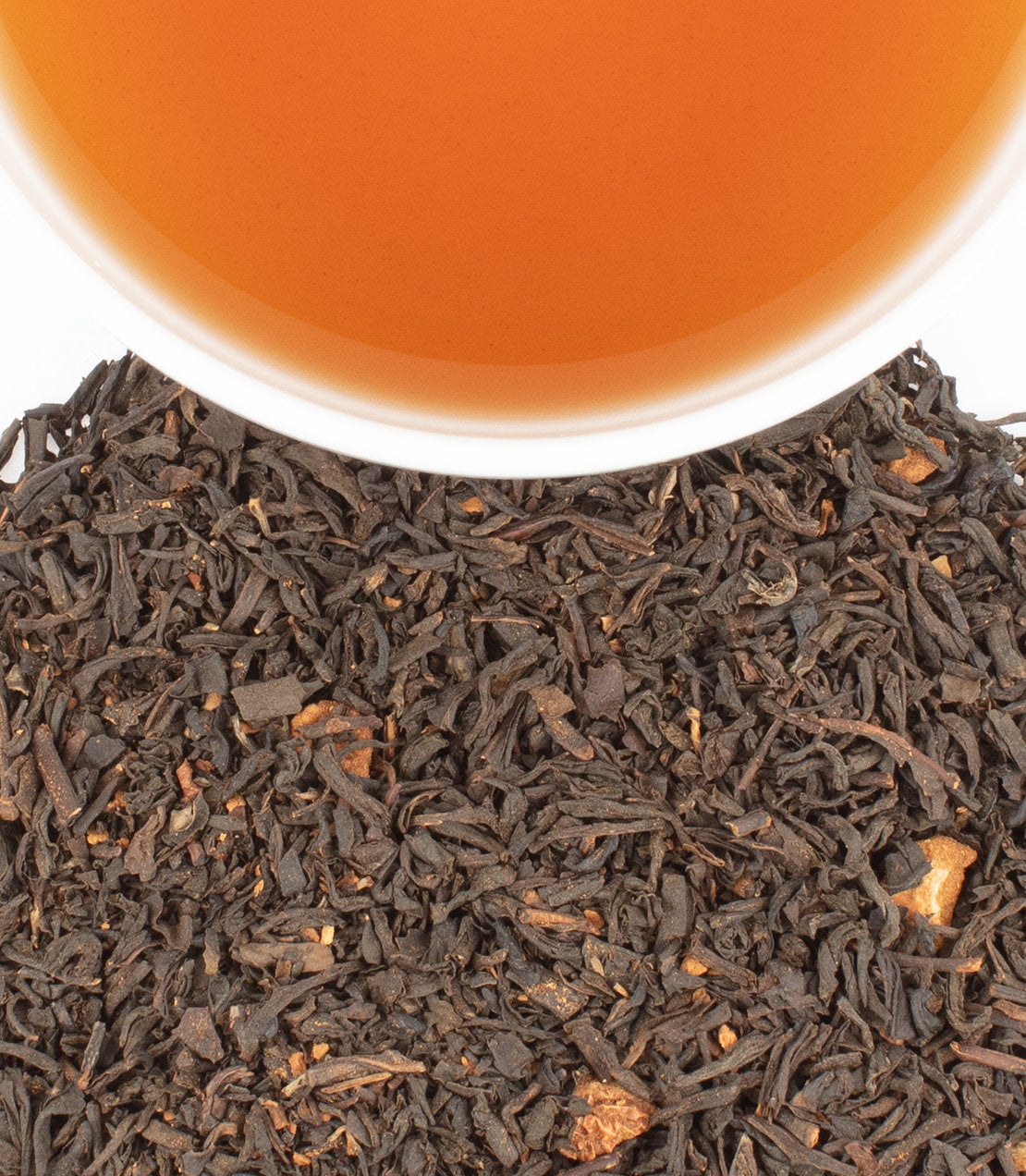 A close-up of loose black tea leaves with apple and cinnamon pieces, alongside a cup of brewed apple cinnamon tea.
