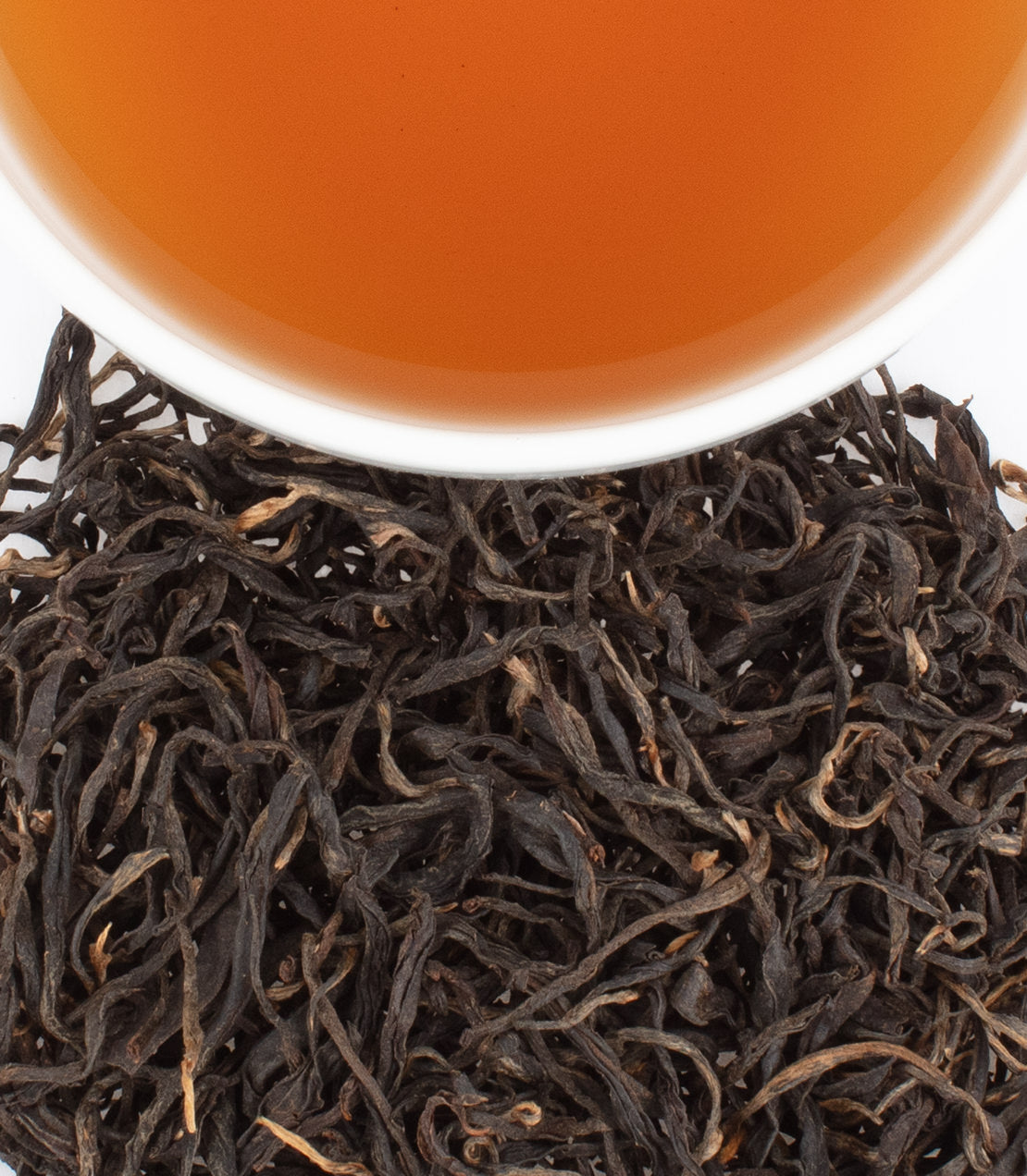 A close-up of BaoMu Wild tea leaves with a cup of brewed tea above, showcasing rich colors and textures.