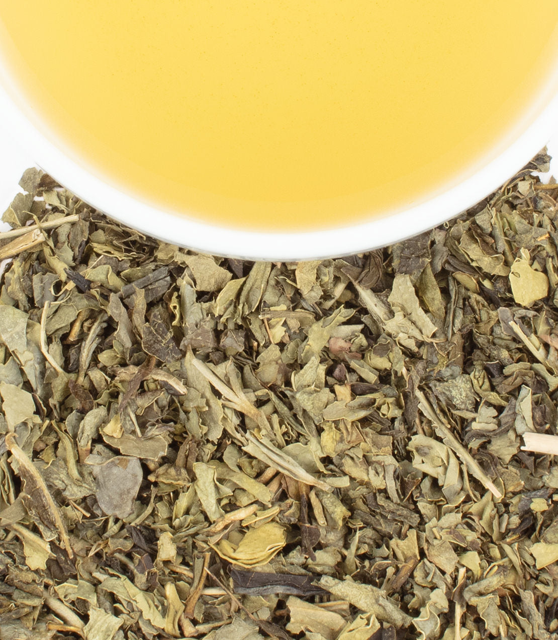 A cup of golden decaf sencha tea above a pile of dried green tea leaves.