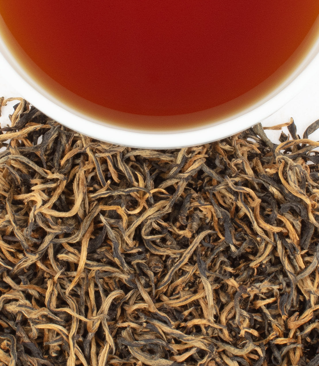 Close-up of Floral Yingde Black tea leaves with a cup of brewed tea above, showcasing rich colors and textures.