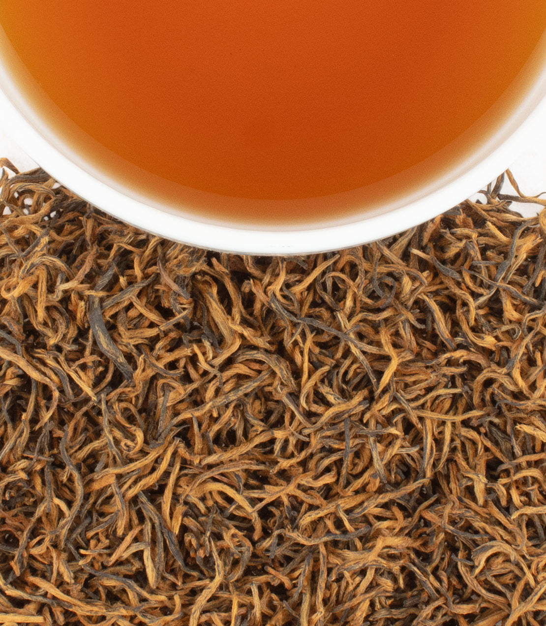 Close-up of Golden Monkey tea leaves with a cup of brewed tea, showcasing rich colors and textures.