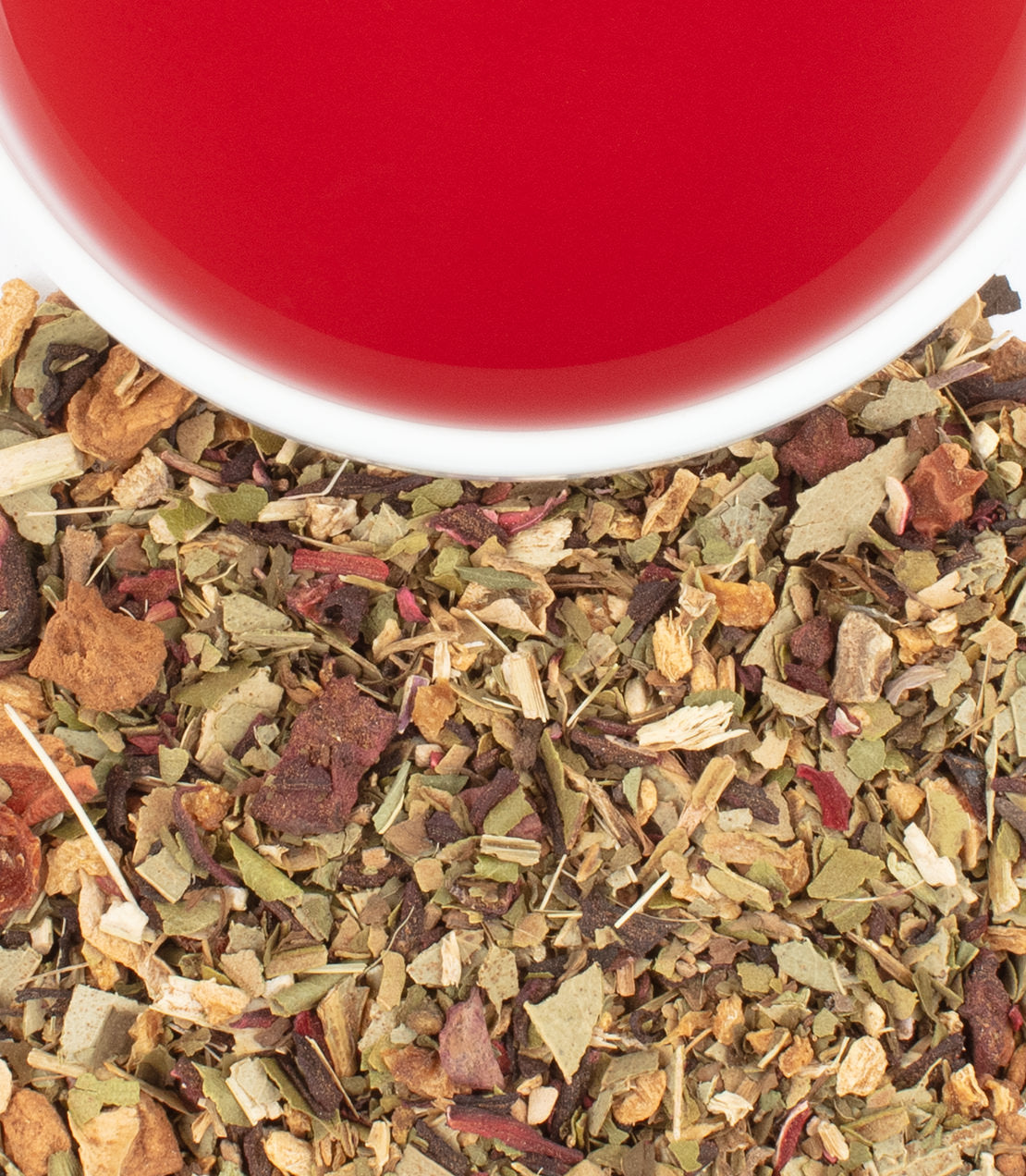 A close-up of organic hibiscus ginger tea leaves with a vibrant red tea in a white cup above.