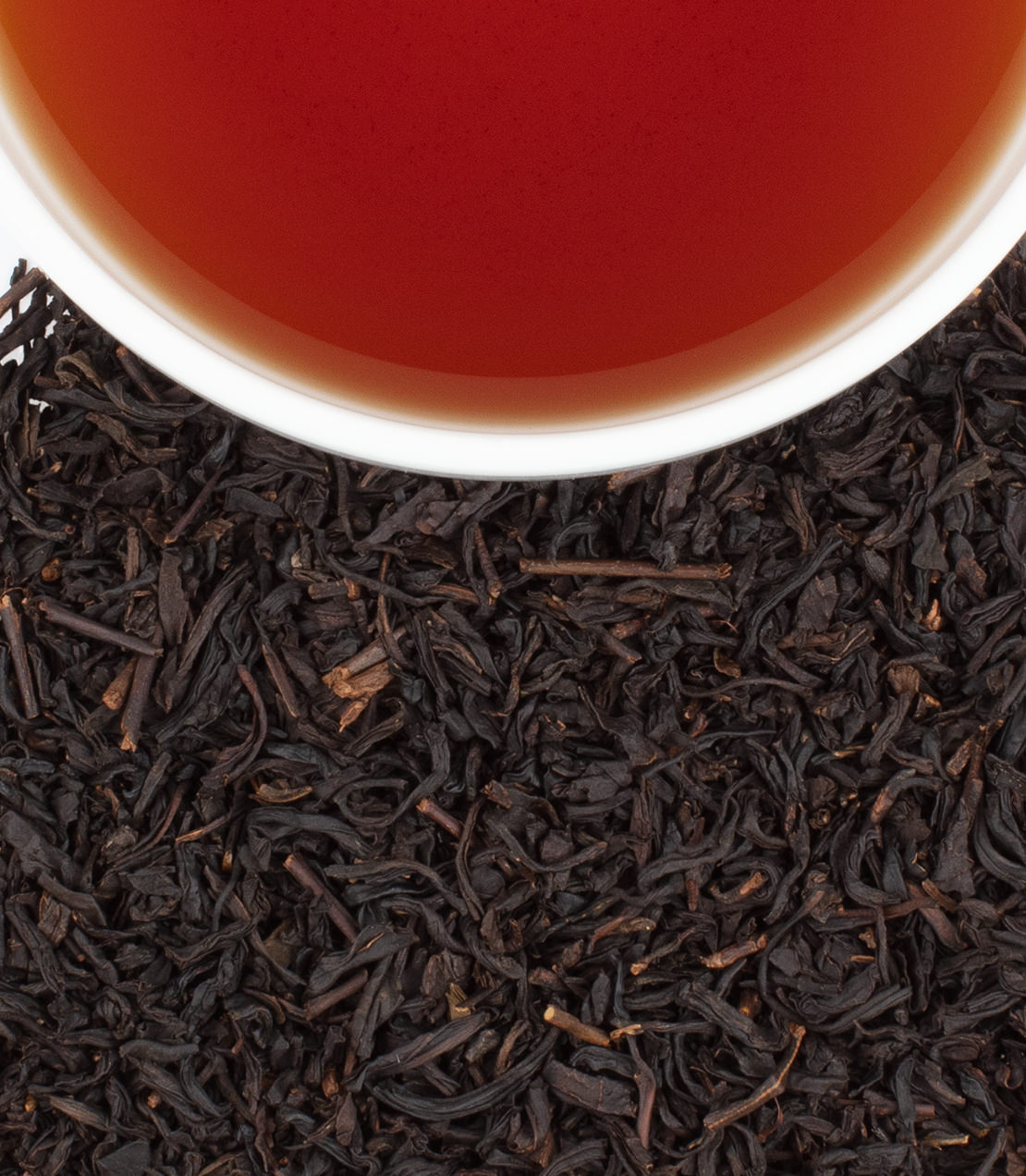Strawberry Vanilla tea in a white cup, surrounded by loose black tea leaves, showcasing a rich amber color.