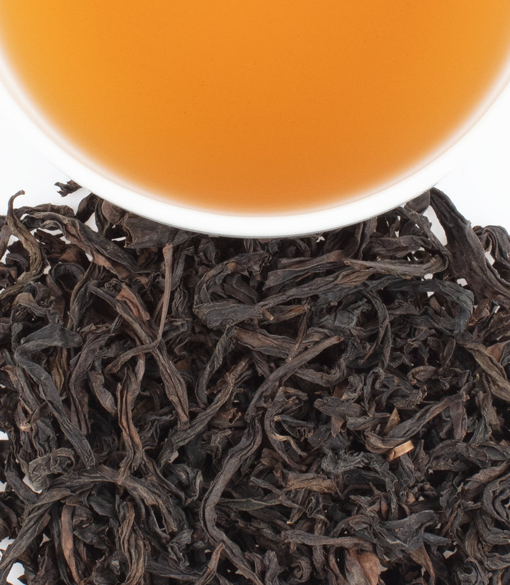 Dried Tong Mu Lapsang tea leaves with a cup of brewed amber tea above, showcasing rich color and texture.