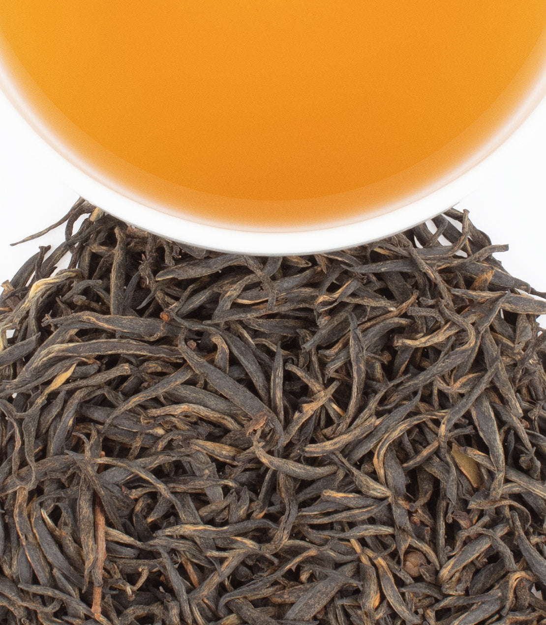 A pile of Jin Jun Mei black tea leaves with a cup of brewed tea above, showcasing its rich amber color.