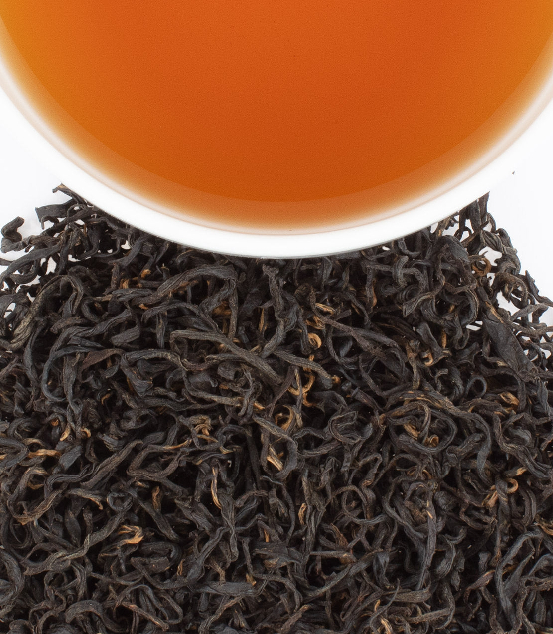 A cup of brewed Wild Tiger Mountain tea above a pile of loose black tea leaves, showcasing rich color and texture.