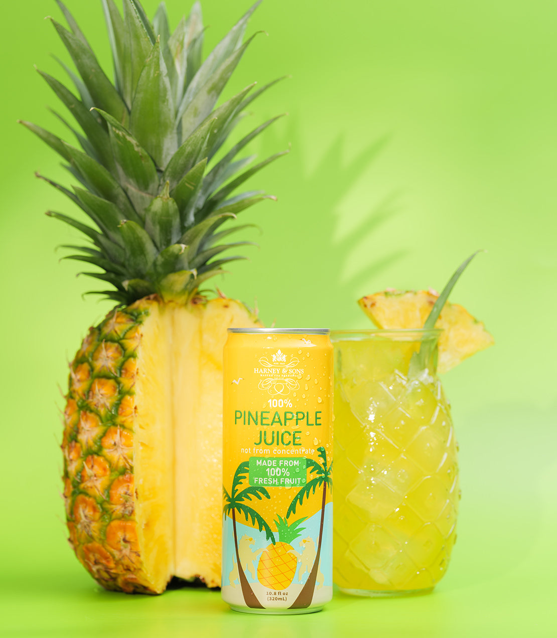 Harney & Sons 100% Pineapple Juice can beside fresh pineapple and a tropical drink on a vibrant green background.