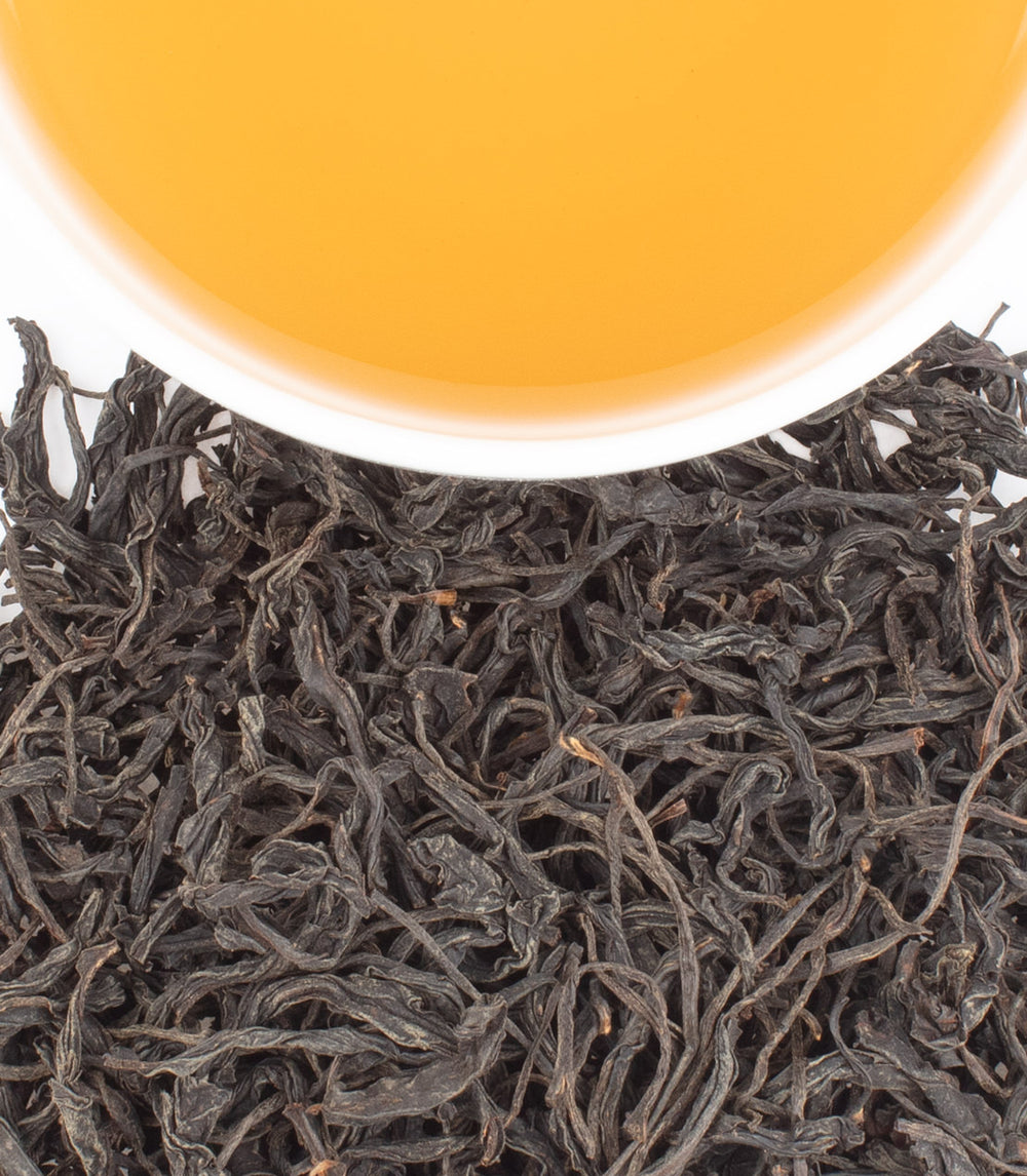 Black Rou Gui tea leaves with a cup of brewed amber tea above, showcasing the rich color and texture.