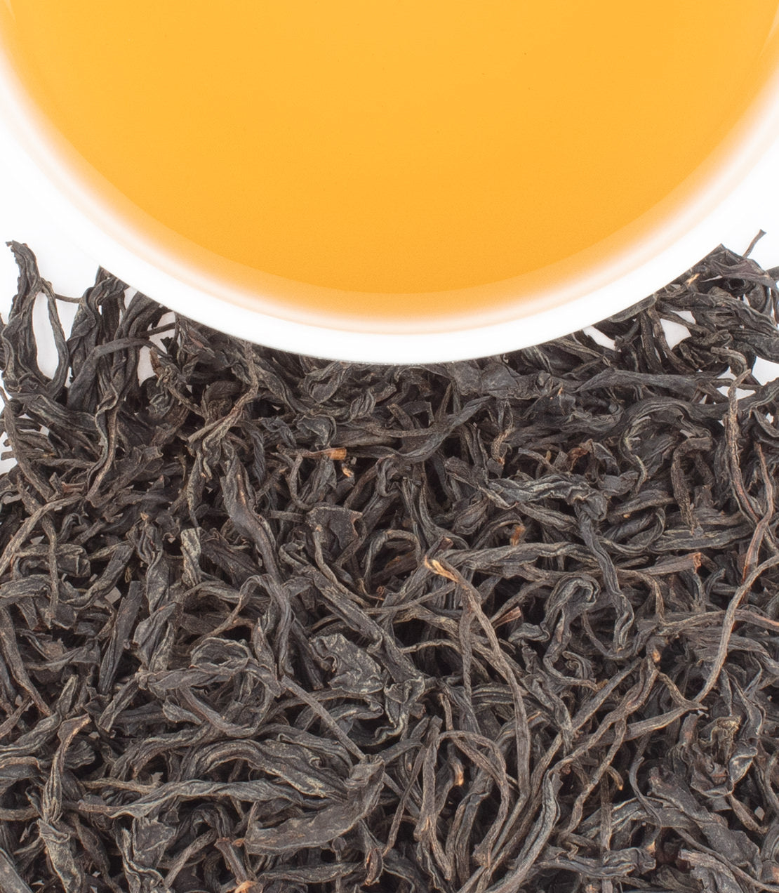 Black Rou Gui tea leaves with a cup of brewed amber tea above, showcasing the rich color and texture.