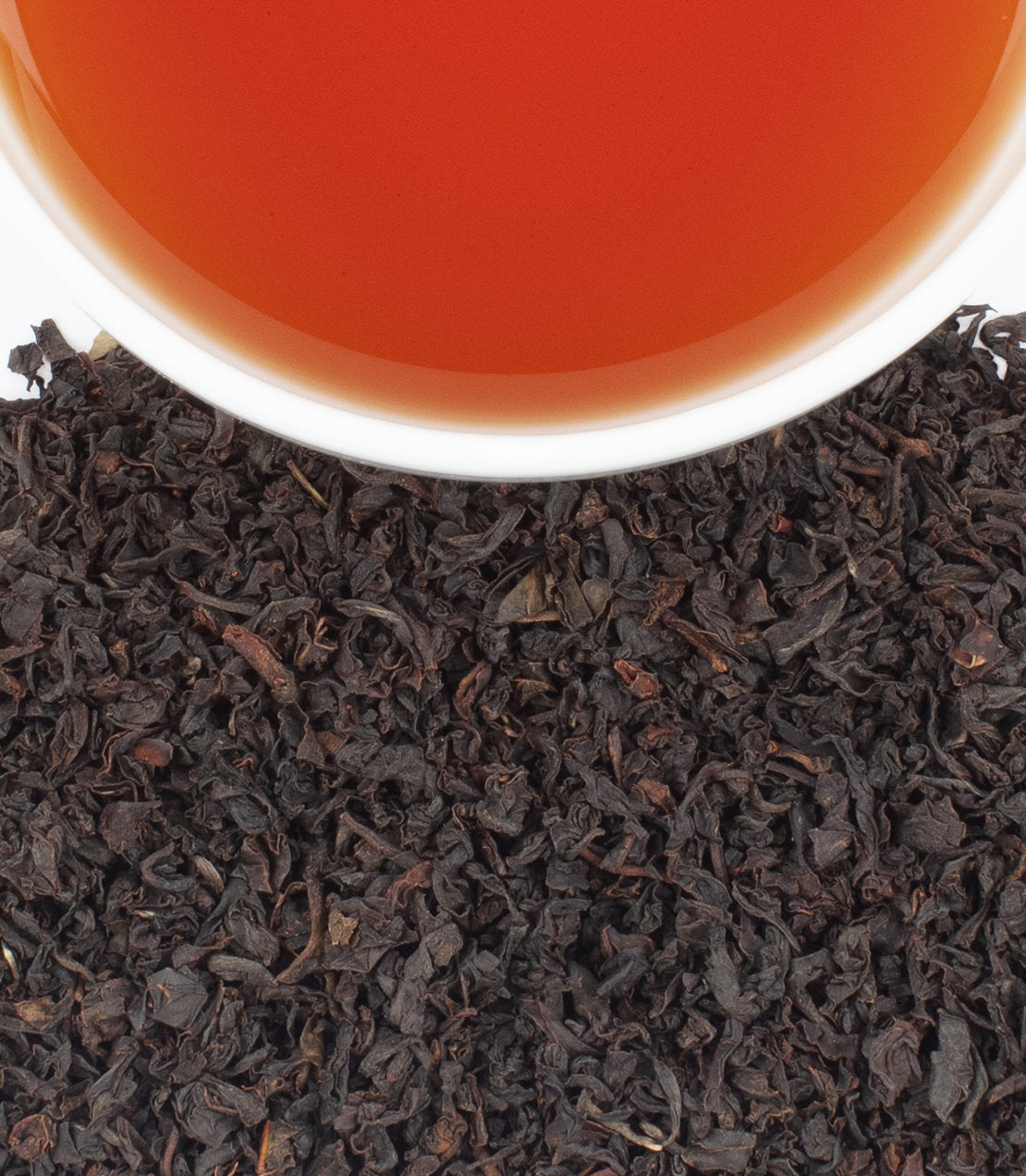 A cup of Chamraj Nilgiri FOP tea above loose black tea leaves, showcasing rich color and texture.