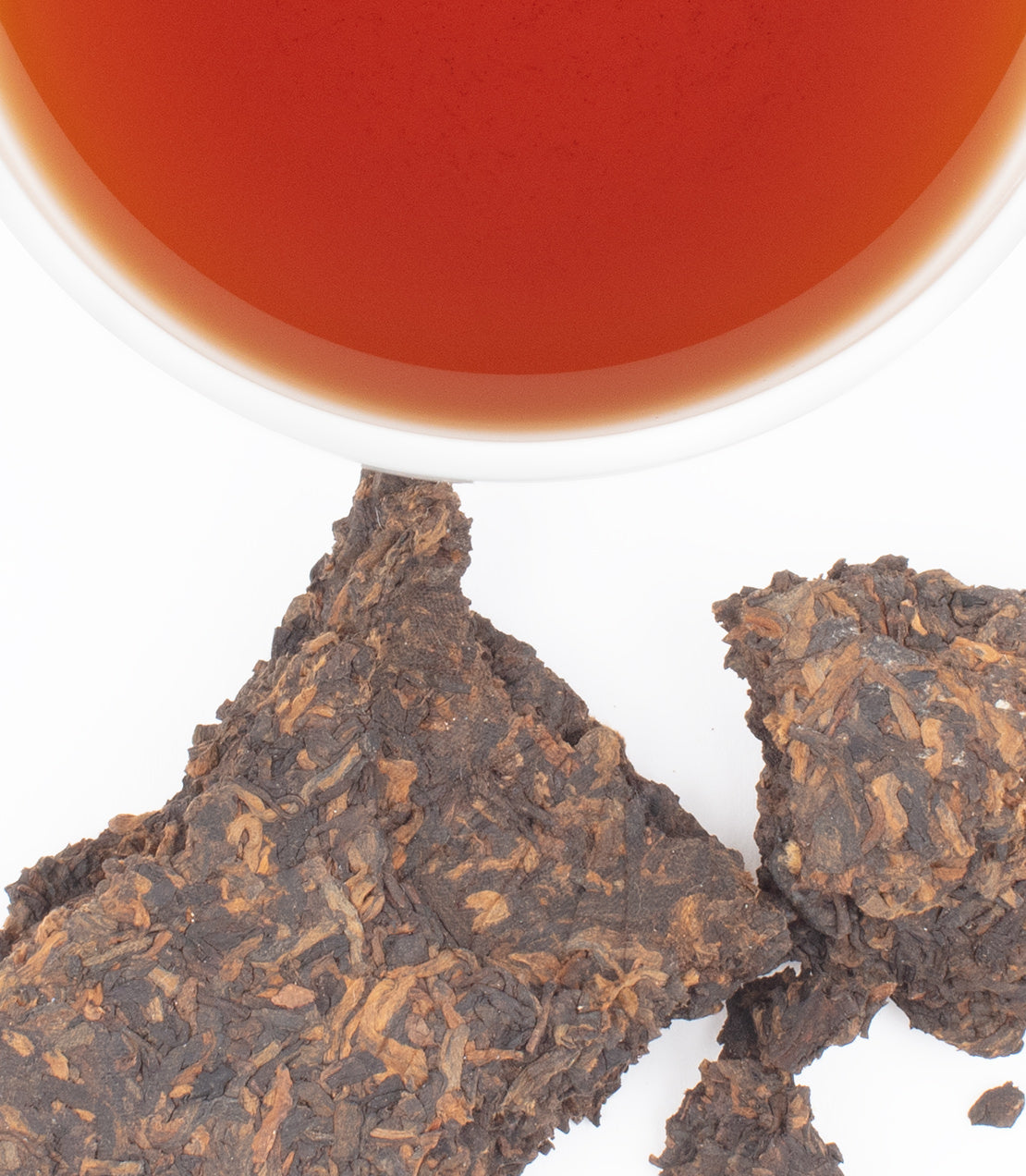 Freshly brewed 2005 Imperial Gold Tip Pu-erh tea in a white cup, surrounded by brown compressed tea leaves.