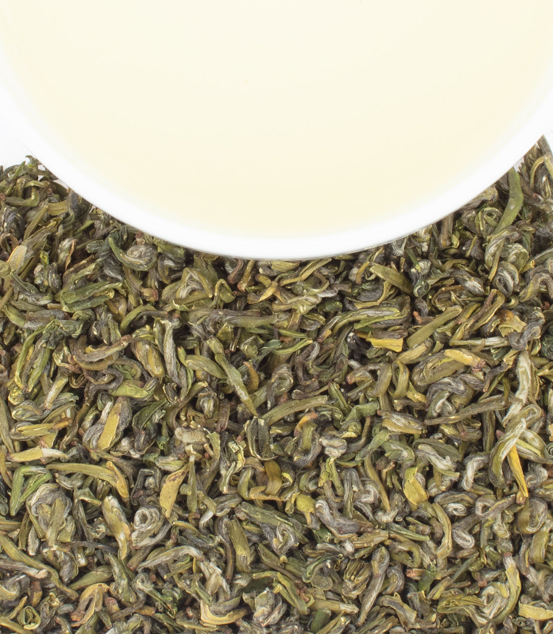 A cup of pale tea rests atop a pile of dried green tea leaves.