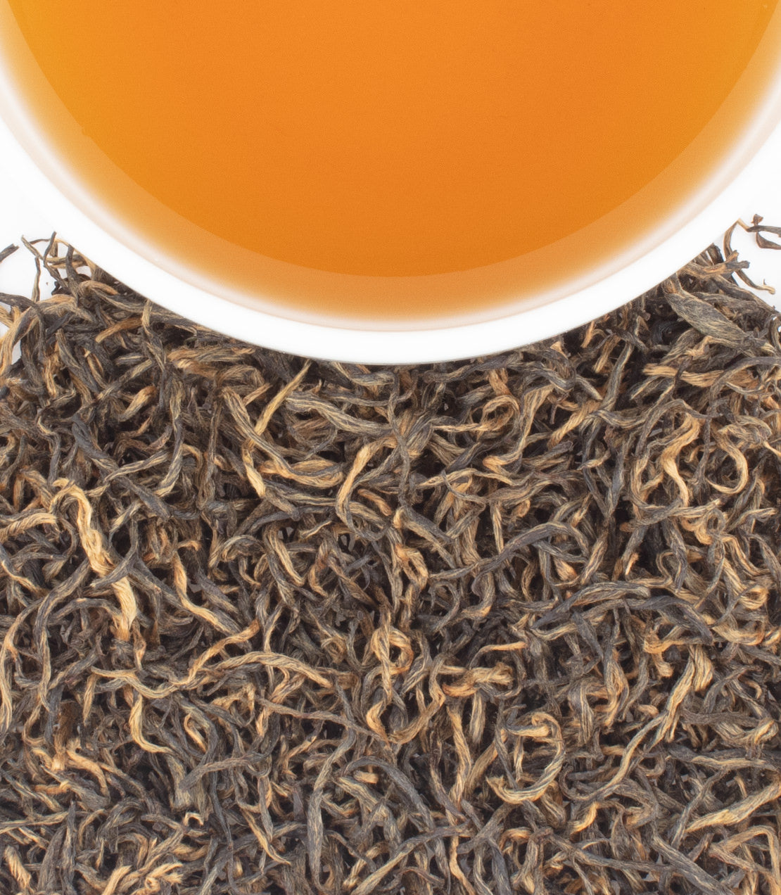A cup of golden tea sits above a pile of dark, twisted loose-leaf tea.