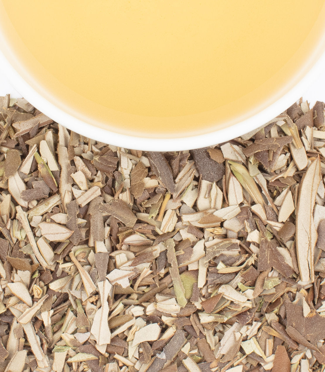 A cup of pale yellow tea sits above a pile of dried, shredded olive leaves on a white surface