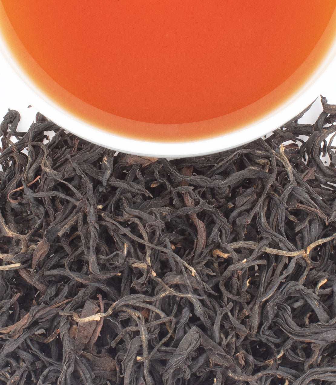 Close-up of loose dark tea leaves with a white cup rim and orange-red tea liquid at the top.