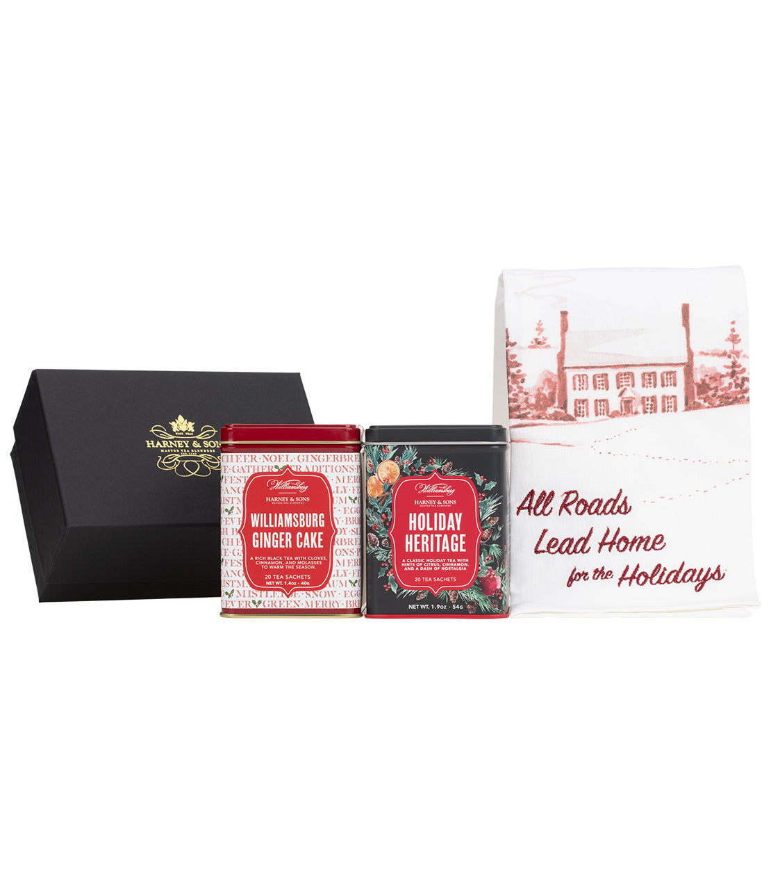 A holiday gift set from Harney & Sons featuring a black presentation box with gold lettering, two tea tins labeled Williamsburg Ginger Cake and Holiday Heritage, and a white tea towel printed with a red house illustration and the phrase 'All Roads Lead Home for the Holidays'.