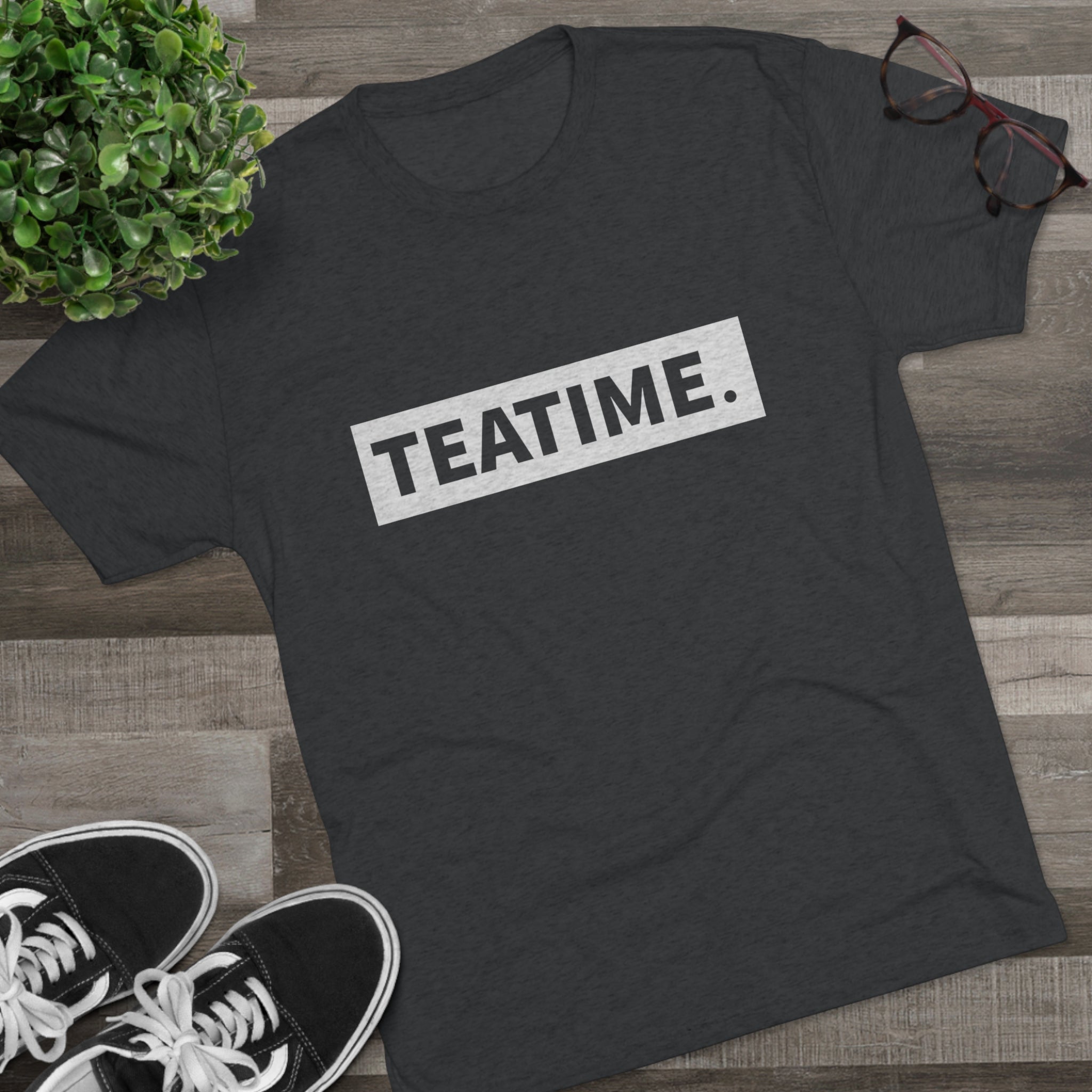 Dark gray graphic tee featuring the word "TEATIME." in bold white letters, styled with casual sneakers and glasses.