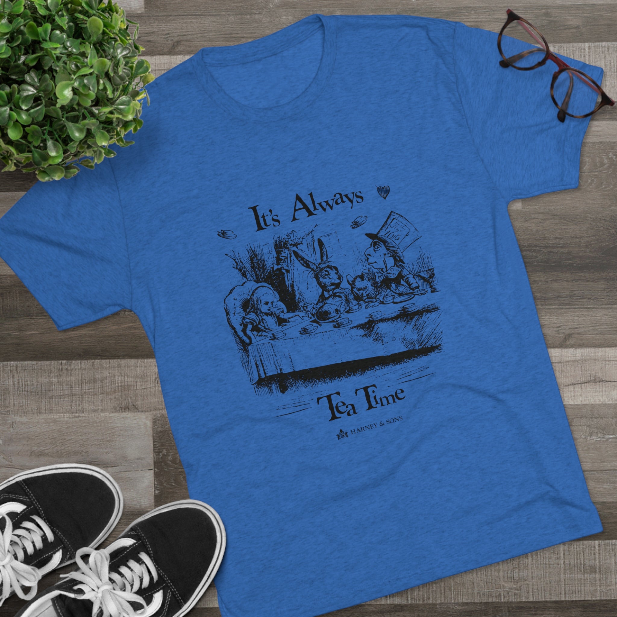 Blue graphic tee featuring "It's Always Tea Time" design with whimsical characters at a tea party. Perfect for tea lovers.