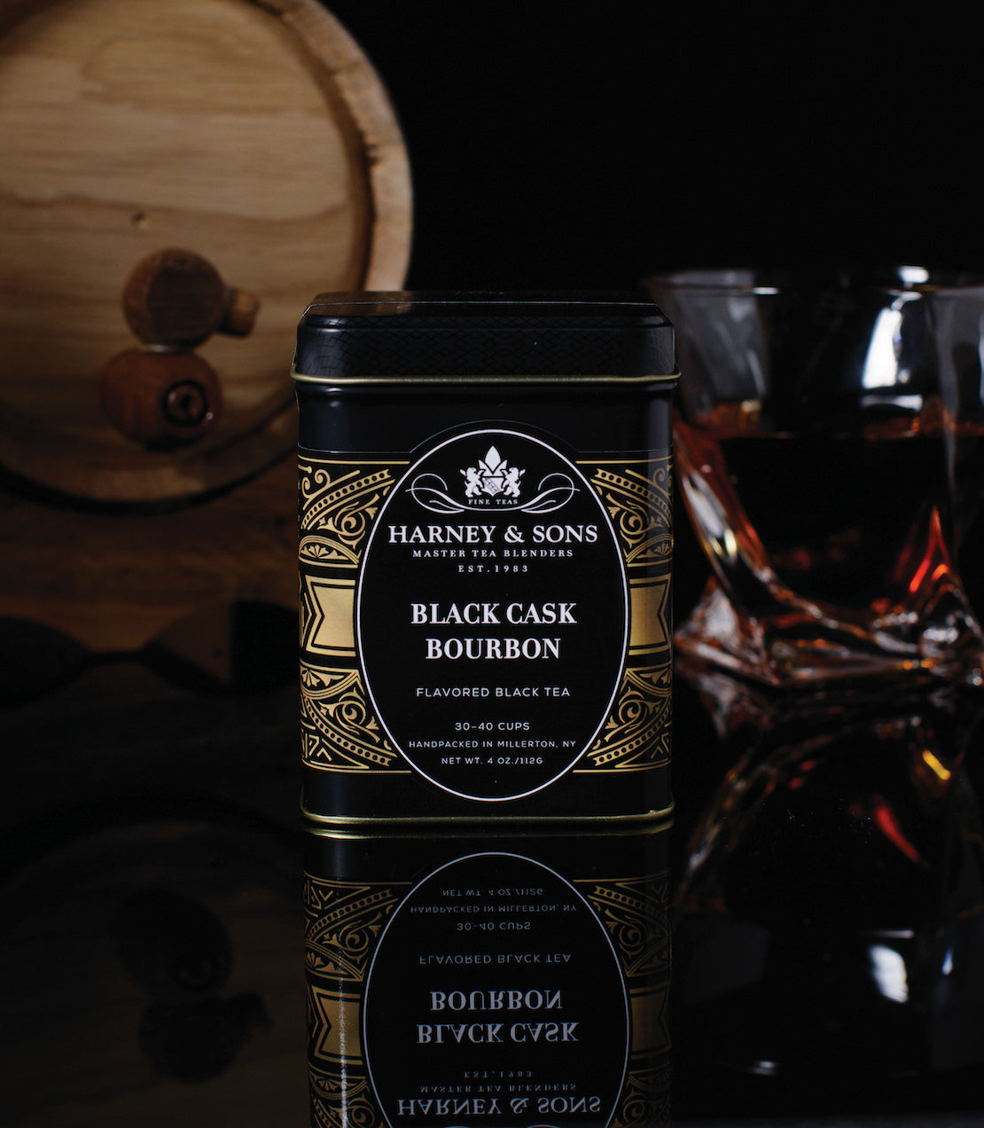 Harney & Sons Black Cask Bourbon flavored black tea tin beside a glass of tea, set against a dark background.