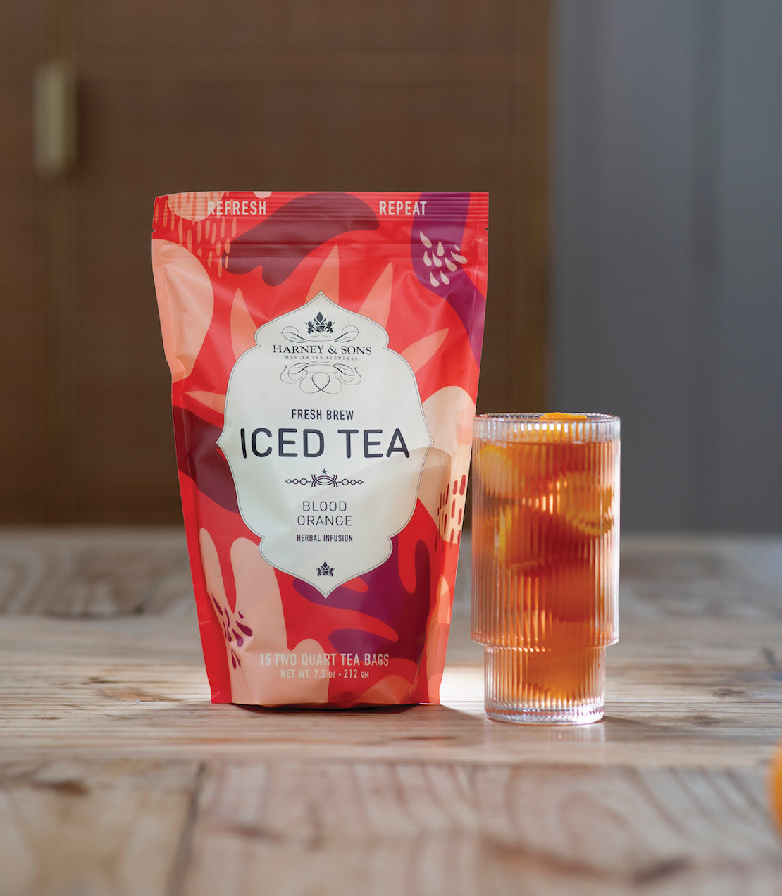 Blood Orange Fresh Brew Iced Tea package beside a glass of iced tea with orange slices on a wooden table.