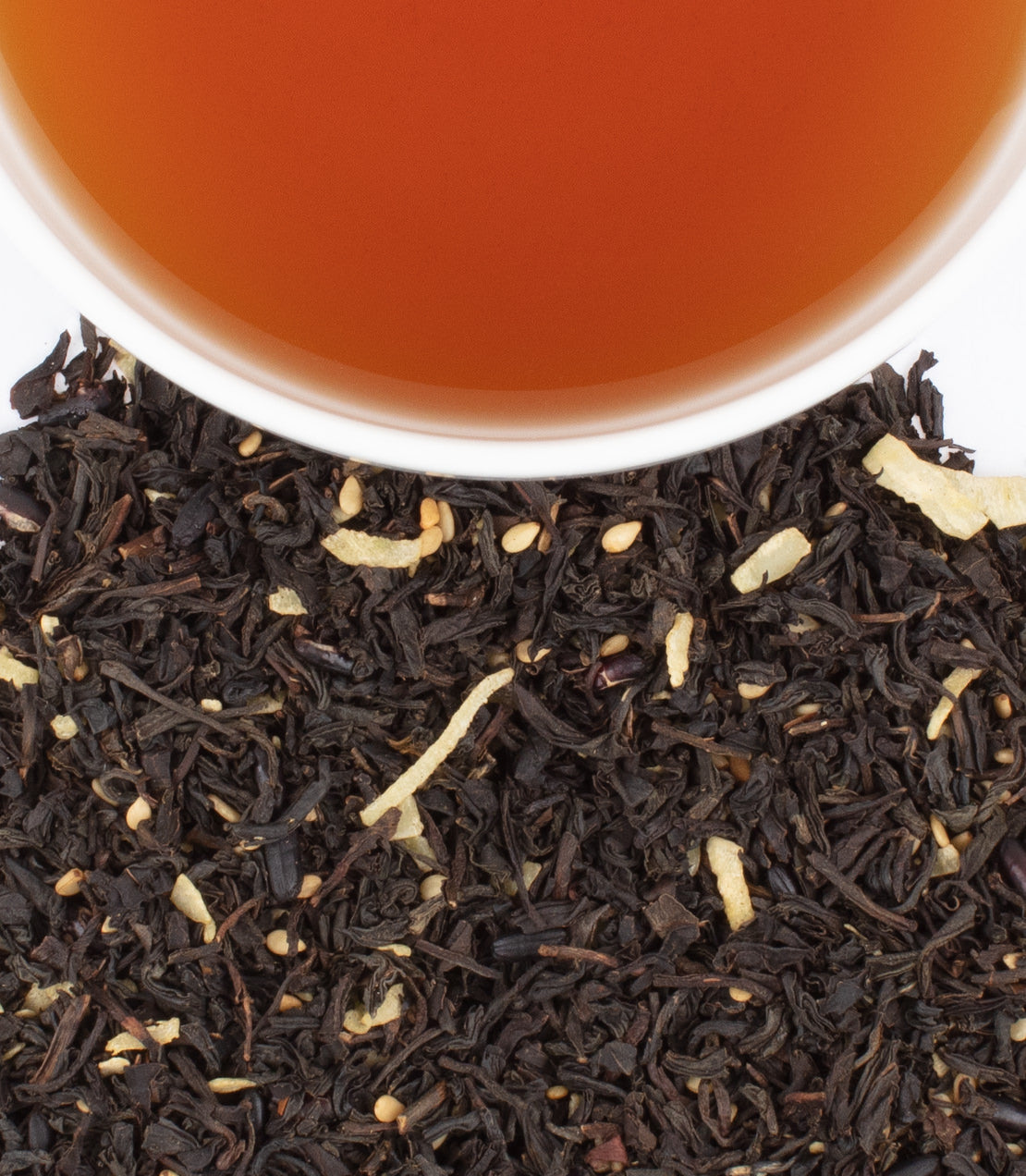 A cup of brewed tea above a pile of loose black tea leaves with dried citrus and sesame pieces, celebrating Lunar New Year 2025.
