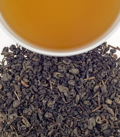 Organic Gunpowder tea sachets with loose tea leaves and brewed tea in a cup above. Perfect for a flavorful brew.