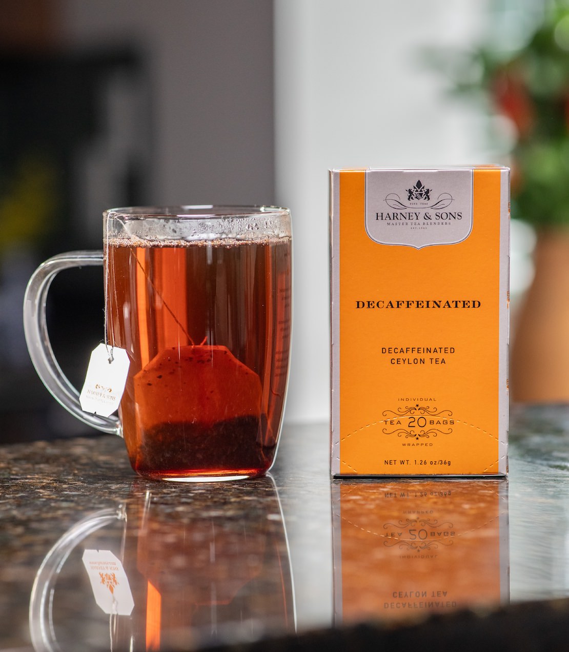 Clear mug with tea and Harney & Sons decaffeinated tea box on a reflective surface
