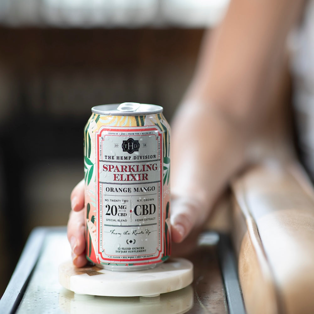 The Hemp Division's Orange Mango Sparkling Elixir with refreshing droplets in a woman's hand