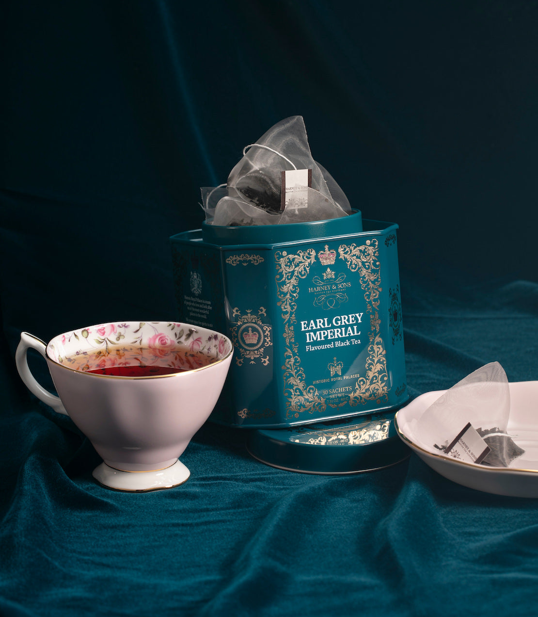 Earl Grey Imperial tea sachets in a decorative tin, accompanied by a plate of cookies on a wooden table.