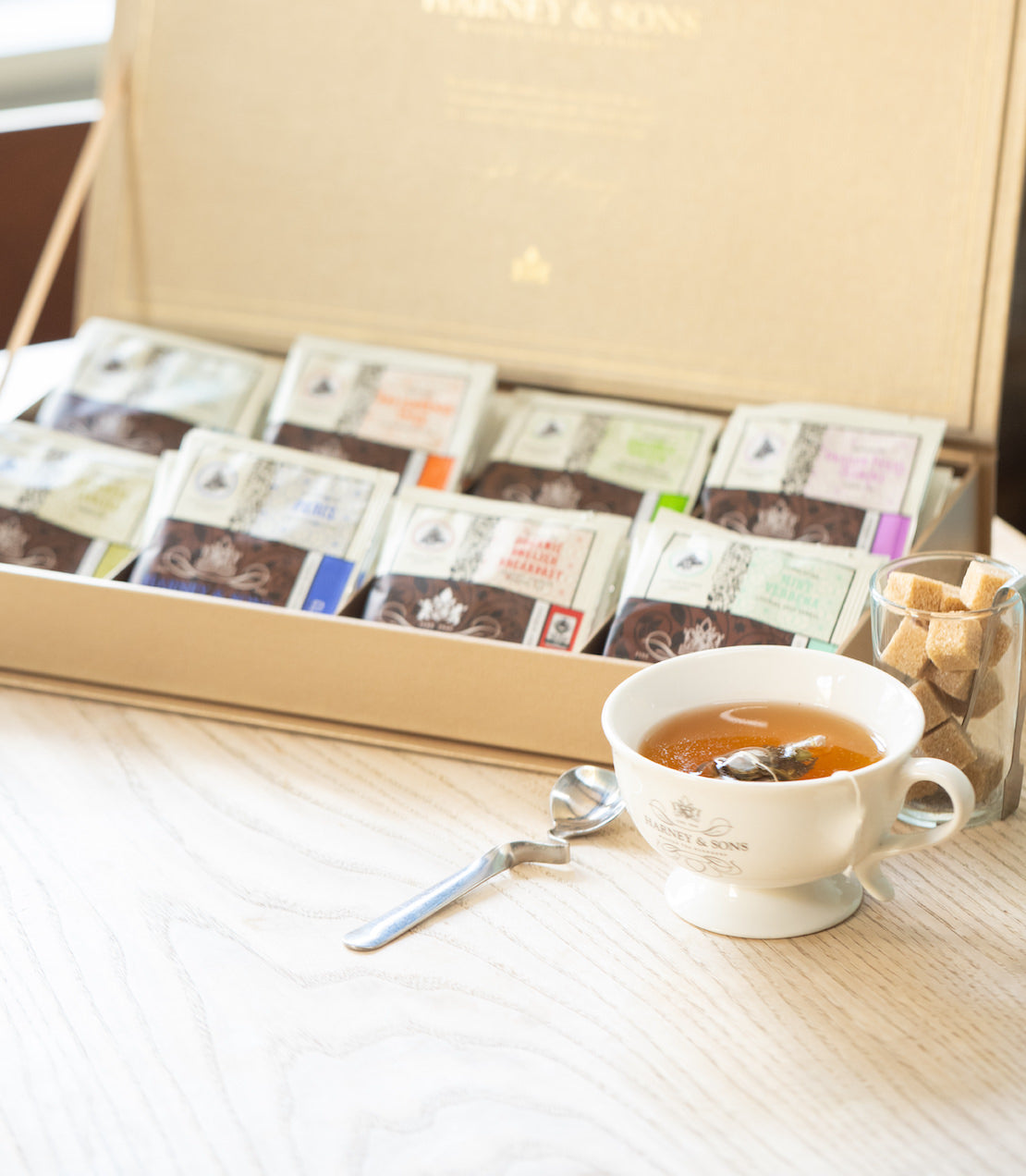 Gold tea chest with eight teas with a cup of tea on a wooden surface.