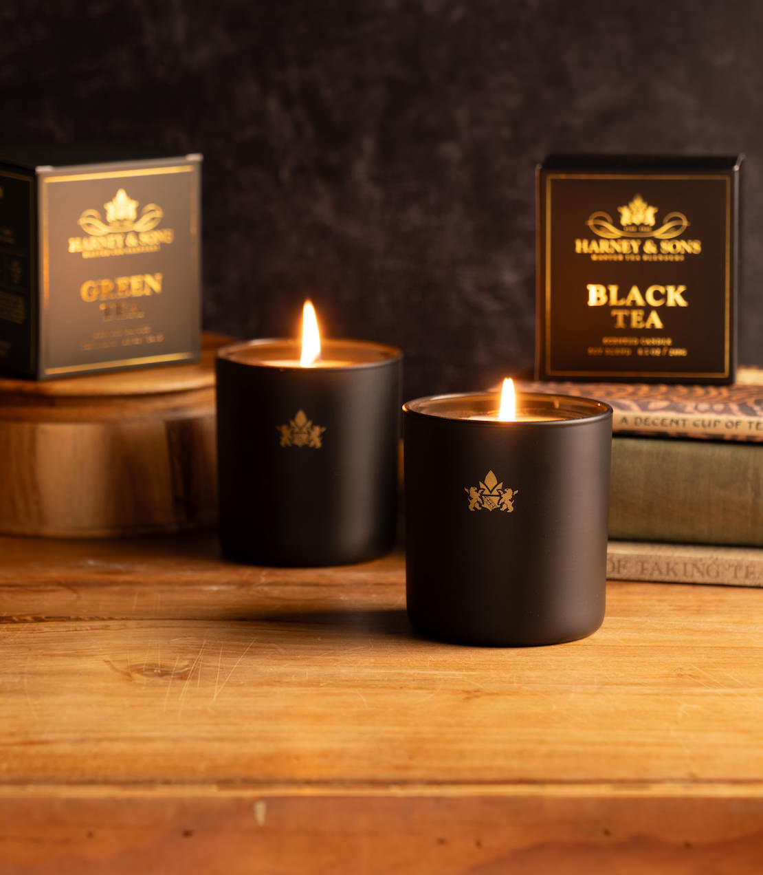 Two lit black candles with Harney & Sons branding on a wooden surface.