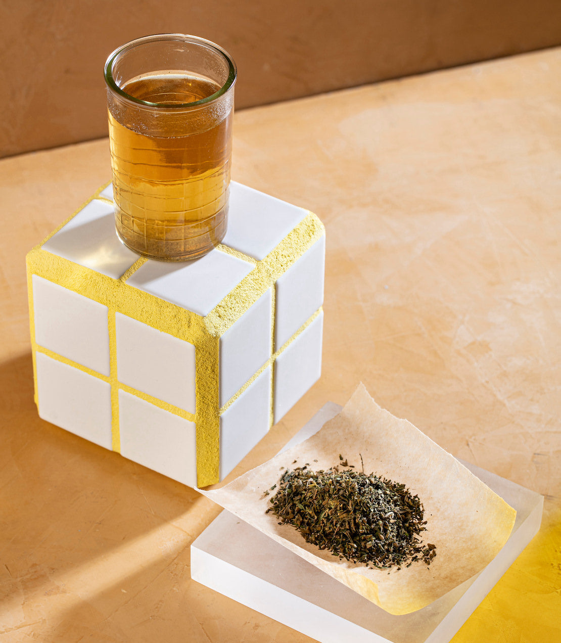 Hemp leaves on parchment paper beside a glass of herbal tea on a textured surface.