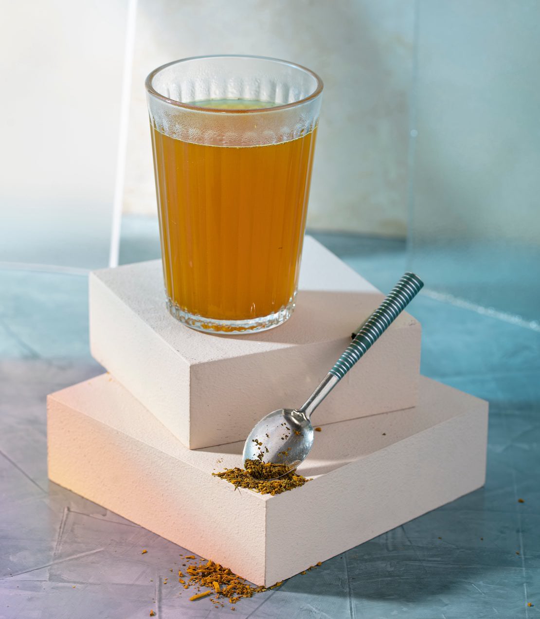 Glass of Hemp Moringa Deep Sleep Wellness Blend on white blocks, with a spoonful of the blend beside it.