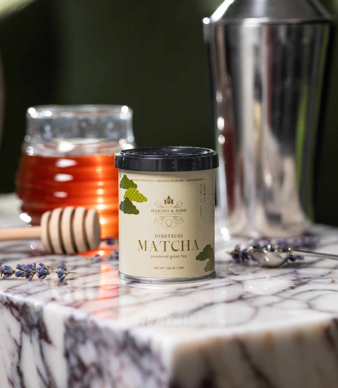 Tin of Jobetsugi matcha on a marble surface with a perfect matcha scoop, iced matcha shaker, honey and lavender.